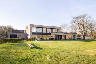 Deze moderne villa uit 2016 is gelegen op een uitzonderlijk breed perceel van ruim een halve hectare (5.016 m²) en combineert hedendaags comfort met een rustige, groene omgeving. Het ontwerp kenmerkt zich door een tijdloze architectuur, waarbij de indrukwekkende raampartijen zorgen voor een uitzonderlijke lichtinval en een naadloze overgang tussen binnen en buiten.<br /><br />De woning is ook praktisch ingericht voor wie wonen en werken wil combineren. Er zijn twee ruimtes voorzien die geschikt zijn voor een professionele activiteit aan huis. <br /><br />In de leefruimte staat ruimtelijkheid en wooncomfort centraal.<br /><br />De keuken is volledig uitgerust met premium toestellen van Gaggenau en een Quooker-kraan. Van hieruit, alsook de gehele leefruimte, geniet u van een weids vergezicht over de zuidoost georiënteerde tuin en de achterliggende natuur. <br /><br />Achter de keuken bevindt zich praktisch een grote berging, die ook toegankelijk is via de carport. Over de gehele woning zijn voldoende maatkasten voorzien, een tweede grote berging en een aparte wasruimte die ook van een douche is voorzien.<br /><br />De woonbeleving wordt verder naar een hoger niveau getild door een slim domoticasysteem, camerabewaking, alarmsysteem en een geïntegreerde muziekinstallatie die doorheen de woning voor de juiste sfeer zorgen.<br /><br />In totaal zijn er vijf slaapkamers en twee badkamers. De master bedroom beschikt over een ensuite badkamer en dressing met zicht op het groen, wat zorgt voor een rustige en aangename sfeer.<br /><br />Met een energielabel A en conforme elektriciteit is ook aan duurzaamheid en technische kwaliteit gedacht, wat het geheel toekomstgericht maakt. Deze lichtrijke villa vormt zo een perfecte balans tussen moderne architectuur, comfort en een unieke ligging in het groen.