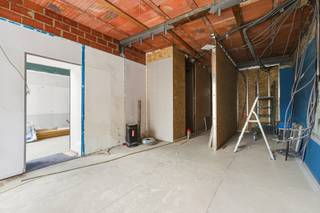 <p>Ben je op zoek naar een ruim handelspand OF project met vergunning voor een appartement met tal van mogelijkheden? Gevonden!</p>
<p>Dit veelzijdige pand biedt vandaag de dag een dubbele opportuniteit: je kan het aankopen en verder uitwerken als handelspand, praktijk of kantoorruimte, MAAR er werd eveneens een vergunning goedgekeurd om het geheel om te vormen tot een volwaardig appartement. Ideaal dus voor ondernemers, investeerders of wie wonen en werken wil combineren. Extra troef: er is geen officiële syndicus, waardoor de maandelijkse lasten bijzonder laag blijven en het plat dak werd langs boven geïsoleerd &amp; afgewerkt met EPDM.</p>
<p>Via de aparte ingang kom je binnen in een ruime inkomhal die perfect kan dienen als ontvangstruimte, wachtruimte of vestiaire &amp; fietsenberging. Links bevindt zich een polyvalente ruimte met veel raampartijen en hoge plafonds. Hier kan eventueel een mezzanine worden gecreëerd. Verder in het pand vind je links twee praktische bergingen en rechts een eerste sanitaire ruimte. Het toilet is reeds aangesloten op de riolering, maar nog geen water of aan- en afvoeren voorzien.</p>
<p>Centraal ligt een bijzonder grote open ruimte die perfect kan functioneren als commerciële hoofdruimte, showroom of praktijkruimte. De elektriciteit werd reeds voorzien. Wie kiest voor de woonfunctie kan hier een riante leefruimte met open keuken realiseren, waarbij mits behoud van de poutrel de tussenmuur kan worden uitgebroken voor een volledig open geheel. Achteraan moet ruimte voorzien worden voor het plaatsen van een glazen wand met patio en buitenkoer, inclusief regenwaterput van 15.000 liter. Aan de rechterzijde is plaats voor bijkomende ruimtes die kunnen ingericht worden als burelen, stockageruimte OF in de woonvariant, één grote en twee kleinere slaapkamers met een tweede badkamer en toilet.</p>