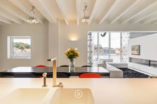 Au cœur de Diest se trouve ce loft d’exception, conçu par PCp Architects. Son architecture se distingue par une esthétique minimaliste en noir et blanc, des lignes épurées et un travail sur mesure soigné. Les rangements intégrés et les techniques dissimulées renforcent le caractère épuré de l’intérieur. Le loft offre 285 m² de surface habitable, complétés par une terrasse sur le toit d’environ 100 m² et une vue panoramique sur la ville.<br /><br />L’espace de vie constitue le cœur du loft et associe de généreuses proportions, de grandes baies vitrées et une cheminée ouverte. La cuisine entièrement équipée comprend notamment un wok intégré. Les appareils électroménagers peuvent être dissimulés derrière un volet à commande électrique, préservant ainsi une esthétique parfaitement épurée.<br /><br />Le même niveau comprend deux chambres, chacune avec sa propre salle de bains, ainsi que de nombreux rangements intégrés.<br /><br />L’étage supérieur est dédié à la vie extérieure. De grandes baies coulissantes relient directement l’intérieur à la terrasse sur le toit. Un bar en fait un espace idéal pour recevoir, tandis qu’une pièce séparée peut être aménagée en bureau ou espace polyvalent.<br /><br />Le loft dispose également d’un garage pour deux voitures, un atout rare en plein centre-ville.