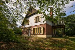 Achter de gevel met de naam ‘Les Hirondelles’ ontdek je een woning waar het karakter van vroeger nog volop aanwezig is. Originele houten deuren, plankenvloeren en grote ramen geven de ruimtes hun warme uitstraling en laten het groen rondom mee deel uitmaken van het interieur.De ruime inkomhal met kachel zet meteen de toon. Van hieruit kom je in de lichte leefruimte met houten vloer en haard. De keuken heeft een opvallende authentieke tegelvloer en geeft toegang naar buiten. Aansluitend ligt de garage met bergruimte. De woning is bovendien volledig onderkelderd.Op de tussenverdieping ligt een slaapkamer met ingemaakte kasten. De eerste verdieping biedt een masterbedroom met toegang tot het balkon, een aangrenzende ruimte die je als dressing met bad kunt inrichten, een derde slaapkamer en een badkamer. Helemaal boven is er nog ruimte voor een vierde slaapkamer, een bureau of een andere invulling die bij je past.‘Les Hirondelles’ is een huis voor wie valt voor authentieke details en graag een plek naar eigen smaak verder vormgeeft.De weergegeven oppervlakte werd overgenomen van het EPC-attest en is louter informatief.