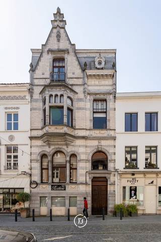 Dit prestigieuze eclectische herenhuis, gelegen in de winkelstraat van Oudenaarde, biedt een unieke kans voor ondernemers die op zoek zijn naar een uitzonderlijk handelspand met een luxueuze uitstraling. Met zijn iconische gevel, één van de meest herkenbare en karaktervolle gevels van de stad, geniet dit pand van een ongeëvenaarde zichtbaarheid en grandeur. De unieke architectuur en de hoogwaardige afwerking zorgen ervoor dat deze eigendom niet alleen een uitstekende commerciële ruimte biedt, maar tevens een stijlvolle woongelegenheid in het hart van de stad.<br /><br />De begane grond is volledig ingericht als een ruime en functionele commerciële ruimte die perfect geschikt is voor diverse doeleinden, zoals een winkel, een showroom of een atelier. De afwerking met granieten elementen draagt bij aan de luxueuze uitstraling, terwijl de royale inkomhal met massief marmeren accenten bezoekers op een indrukwekkende manier verwelkomt. Daarnaast beschikt deze verdieping over een apart gastentoilet, een bijkeuken, een technische ruimte en een kluis. Twee trappen bieden toegang tot ruime kelders, die ideaal kunnen dienen als opslagruimte of voorraadbeheer.<br /><br />Het commerciële gedeelte heeft directe toegang tot een sfeervolle binnenkoer, wat niet alleen een aangename werkruimte creëert, maar tevens een bijkomende troef is voor zowel klanten als medewerkers. Bovendien beschikt het pand over een zonnige tuin, een dakterras en een ruime garage met carport, die toegankelijk zijn via een achterliggende straat. Deze extra voorzieningen vormen een onschatbare meerwaarde voor een handelspand in het centrum van Oudenaarde en verhogen het gebruiksgemak voor zowel professioneel als privégebruik.<br /><br />Naast de commerciële mogelijkheden biedt dit eigendom eveneens een ruime en stijlvolle woongelegenheid, waarin authentieke charme en hedendaags comfort harmonieus samenkomen. De imposante inkomhal leidt naar een elegant salon met open haard, een eetkamer en een volledig uitgeruste keuken met een praktische berging. Op de tussenverdieping bevinden zich de wasplaats en de eerste badkamer. De eerste en tweede verdieping omvatten samen vier ruime slaapkamers en twee badkamers, waardoor deze woning bijzonder geschikt is voor ondernemers die hun professionele activiteiten wensen te combineren met een luxueus en comfortabel privéleven.<br /><br />Dankzij de uitzonderlijke ligging, de stijlvolle afwerking en de historische uitstraling vormt dit pand een unieke opportuniteit voor wie op zoek is naar een prestigieus handelspand met woonst in het centrum van Oudenaarde. De combinatie van een exclusieve commerciële ruimte met een ruime en comfortabele woongelegenheid biedt niet alleen een uitstekende zichtbaarheid en bereikbaarheid, maar verzekert ook een ongeëvenaarde uitstraling voor iedere onderneming. Voor meer informatie of een bezichtiging kunt u contact met ons opnemen.