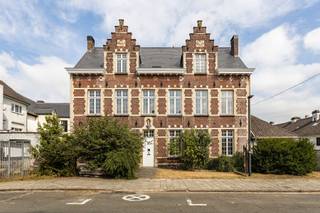 Op een toplocatie op het authentieke Begijnhof in het centrum van Aalst staat dit statige herenhuis op een perceel van 2a 23ca. Met een in 2025 hoogwaardig vernieuwd dak is de belangrijkste investering al achter de rug, wat een uitstekende basis biedt voor wie het interieur naar eigen smaak wil renoveren. Via de ruime inkomhal betreedt u het gelijkvloers van 140 m², waar zich drie grote polyvalente ruimtes en een eenvoudige keuken bevinden met zicht op de fijne, noordwestelijk georiënteerde stadstuin. De eerste verdieping beschikt over een nachthal en vijf volwaardige kamers die naar wens kunnen worden ingericht. Daarnaast biedt de imposante zolder van 128 m² onder het nieuwe dak nog enorm veel extra uitbreidingsmogelijkheden, en is er een kelder van 26 m² aanwezig. Dankzij de ligging in woongebied en de indeling leent het pand zich perfect voor een gezinswoning, kantoor of de uitoefening van een vrij beroep, en dat op wandelafstand van scholen, winkels en het openbaar vervoer.