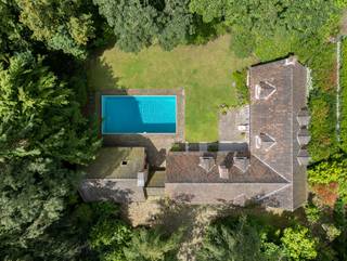 <p>In de uiterst gegeerde en groene <span>Solhofomgeving in Aartselaar</span> bevindt zich deze charmante <span>jaren 70-hoeve</span> op een uitzonderlijk rustig en residentieel perceel. Solhof staat bekend als een van de meest geliefde woonomgevingen van Aartselaar, met een uitgesproken groen karakter, statige dreven en een aangename combinatie van privacy, natuur en vlotte bereikbaarheid. Het gemeentelijk park Solhof ligt in de buurt en ook het centrum van Aartselaar, verbindingswegen en de as richting Antwerpen zijn vlot bereikbaar.<br /><br /><span>Deze karaktervolle woning ademt authenticiteit en sfeer. De architectuur in hoevestijl, de warme bakstenen gevels, de charmante luiken, de zichtbare houten balken en de traditionele materiaalkeuzes geven het geheel een tijdloze uitstraling. De woning is discreet ingebed in een groene, volwassen tuinomgeving, waardoor rust en privacy hier centraal staan.</span></p>
<p>Bij aankomst valt meteen de idyllische setting op: een lange oprijlaan in kasseiverharding, omringd door bomen en volwassen beplanting, leidt naar de woning. De hoeve is opgebouwd rond een ruim volume met verschillende dakpartijen en bijgebouwen, wat het eigendom een authentiek en bijna landelijk cachet geeft.</p>
<p>Aan de tuinzijde geniet de woning van een bijzonder aantrekkelijk buitengebeuren. Het ruime gazon, de omliggende bomen en het <span>ingegraven zwembad</span> zorgen voor een echt vakantiegevoel in eigen huis. Het terras en de poolzone vormen een ideale plek om in alle rust te ontspannen of gasten te ontvangen in een unieke groene setting.</p>
<p>Binnenin wordt de charme van de woning verdergezet. De inkomhal maakt meteen indruk met haar dubbele hoogte, terracotta vloer, houten trap en zichtbare balkstructuren. Deze elementen geven de woning een warme, authentieke ziel en zorgen voor een sterke eerste indruk. Ook in de leefruimtes komen karakter en volume mooi samen: houten plafondelementen, robuuste balken, warme vloeren en grote raampartijen creëren een uitnodigende en huiselijke sfeer.</p>
<p>De eetkamer straalt klasse en gezelligheid uit, met haar rustieke afwerking en aangenaam contact met het groen buiten. De bovenverdieping biedt eveneens heel wat charme, met prachtige daklijnen en een indrukwekkende open balkenstructuur die de ruimtes extra karakter geeft. Hierdoor leent de woning zich perfect voor wie houdt van een interieur met persoonlijkheid, authenticiteit en een landelijke elegantie.</p>
<p>Deze woning biedt een zeldzame combinatie van <span>ligging, charme, volume en potentieel</span>. Ze is ideaal voor liefhebbers van karaktervastgoed die op zoek zijn naar een residentieel gelegen eigendom met een warme uitstraling, veel privacy en een sterke architecturale identiteit.</p>