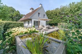 Op een uitzonderlijke locatie in Groenendijk-Oostduinkerke, op de grens met Nieuwpoort-Bad en op slechts 400 meter van het strand, bevindt zich deze charmante Mi Casa-woning op een prachtig perceel van maar liefst 1.271 m². De combinatie van de unieke ligging, de warme houtskeletbouw en de groene, zonnige tuin creëert een heerlijk beach house-gevoel waar rust, ruimte en de kust naadloos samenkomen.<br />De woning, gebouwd in 2001, verwelkomt u via een ruime inkomhal met apart gastentoilet. De lichtrijke woonkamer met gezellige haardcassette vormt het hart van de woning en geniet dankzij de grote raampartijen van een prachtig zicht op het zonnige terras, de fraai aangelegde tuin en de sfeervolle vijver. Aansluitend bevindt zich de eetplaats en de open keuken, die samen zorgen voor een aangename en open leefomgeving.<br />Op het gelijkvloers beschikt de woning verder over een ruime garage met praktische kelder, een carport en een afzonderlijke tuinberging.<br />De bovenverdieping omvat drie volwaardige slaapkamers, waaronder een royale master bedroom uitgerust met een airco voor optimaal comfort. De badkamer is ingericht met een dubbele wastafel, een ligbad en een afzonderlijke douche. Daarnaast bevindt zich op deze verdieping nog een apart toilet en een gedeeltelijke zolderberging die extra opbergruimte biedt.<br />Ook op technisch vlak scoort deze woning bijzonder goed. Zo is ze uitgerust met een regenwaterput van 10.000 liter en zonnepanelen, wat bijdraagt aan een duurzame en energiezuinige woonervaring.<br />Deze authentieke Mi Casa-woning in houtskeletbouw straalt warmte en karakter uit en vormt een zeldzame opportuniteit voor wie op zoek is naar een instapklare gezinswoning of een tweede verblijfplaats op wandelafstand van zee. Dankzij de uitzonderlijke ligging tussen de duinen, het strand, Groenendijk en Nieuwpoort-Bad geniet u hier elke dag van een permanent vakantiegevoel aan de Belgische kust. EPC: 211 kWh/m². Vraagprijs: 795000€