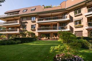<p>Dit uitzonderlijk ruime en instapklare gelijkvloers appartement combineert een royale woonoppervlakte met een hoogwaardige afwerking, een aangename lichtinval en een doordachte indeling. Met ca. 200 m² bewoonbare oppervlakte, een ruim en zonnig terras en rechtstreekse toegang tot de prachtig aangelegde parktuin met vijver, biedt deze unieke eigendom een bijzonder aangename woonbeleving.</p>
<p>Het appartement beschikt over drie volwaardige slaapkamers, twee badkamers, een aparte wasplaats en bijkomende bergruimte in de kelder. Daarnaast zijn er twee ruime parkeerplaatsen in de ondergrondse garage.</p>
<p><strong>Indeling</strong></p>
<p>Via de stijlvolle en lichtrijke gemeenschappelijke inkomhal bereikt u het appartement. De centrale inkomhal beschikt over een vestiaire en gastentoilet en biedt toegang tot zowel de leefruimtes als de keuken.</p>
<p>De luxueus afgewerkte keuken is uitgerust met kwalitatieve inbouwtoestellen, waaronder een vaatwasser, koelkast, diepvriezer, combi-oven en stoomoven.</p>
<p>De bijzonder ruime leefruimte is afgewerkt met tijdloze eiken parket en omvat een sfeervolle eethoek, een gezellige tv-hoek en een aparte leesruimte. Dankzij de grote raampartijen geniet de ruimte van een overvloed aan natuurlijk licht en een prachtig zicht op de aangelegde tuin en vijver. Vanuit de leefruimte is er rechtstreeks toegang tot het ruime, zonnige terras.</p>
<p>Via de nachthal bereikt u de drie volwaardige slaapkamers. Eén van de kamers is momenteel ingericht als bureau en beschikt over een aansluitende wasplaats. De twee overige slaapkamers beschikken elk over een privatieve buitenruimte en sluiten aan op respectievelijk een douchekamer en een badkamer.</p>
<p><strong>Bijzonderheden</strong></p>
<ul>
<li>
<p>Instapklaar en luxueus afgewerkt gelijkvloers appartement van ca. 200 m²</p>
</li>
<li>
<p>Ruim en zonnig terras met zicht op de prachtig aangelegde parktuin en vijver</p>
</li>
<li>
<p>Drie volwaardige slaapkamers</p>
</li>
<li>
<p>Twee badkamers</p>
</li>
<li>
<p>Volledig voorzien van kwalitatief maatwerk en ingemaakte kasten</p>
</li>
<li>
<p>Hoogwaardige afwerking met onder meer eiken parket en natuursteen</p>
</li>
<li>
<p>Uitstekende beveiliging met alarmsysteem</p>
</li>
<li>
<p>Twee ruime parkeerplaatsen in de ondergrondse garage</p>
</li>
<li>
<p>Extra bergruimte in de kelder</p>
</li>
</ul>