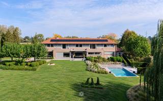 <h1><span>Architecturale villa met zwembad op uitzonderlijk privédomein in de Vlaamse Ardennen</span></h1><p><span>VLAAMSE ARDENNEN</span><span> Sommige woningen imponeren door hun grandeur, andere door de rust die ze uitstralen. Hier komen beide op uitzonderlijke wijze samen.</span></p><p><span>Discreet verscholen in het groen van de Vlaamse Ardennen bevindt zich een bijzonder architecturaal eigendom waar ruimte, privacy en verfijning centraal staan. Op een zuidgericht domein van maar liefst 70a90ca ontvouwt zich een statige villa met circa 650 m² bewoonbare oppervlakte, ontworpen volgens een uitgesproken horizontale en symmetrische architectuur.</span></p><p><span>Wat zich aan de straatzijde eerder ingetogen presenteert, onthult eenmaal binnen zijn ware grandeur. Royale leefvolumes, indrukwekkende zichtlijnen en grote raampartijen creëren een uitzonderlijk gevoel van ruimte en licht. De woning opent zich volledig naar een prachtig aangelegd privépark, waar slingerende paden, strak geschoren hagen, volwassen bomen en drie vijvers een harmonieus geheel vormen. Centraal in dit groene decor ligt het verwarmde zwembad van 6 x 11 meter, afgewerkt in glasmozaïek.</span></p><p><span>Ook binnen weerspiegelt elk detail de kwaliteit van het eigendom. Massief parket, Portugese witsteen, marmer, natuursteen en verfijnd maatwerk zorgen voor een tijdloze elegantie. De royale leefruimte met stijlvolle doorkijkhaard vormt het hart van de woning en sluit aan op een afzonderlijke eetkamer en een bijzonder ruime, hoogwaardig uitgeruste Vossaert-leefkeuken. Een wintertuin, gezellige TV- en speelkamer en talrijke discreet geïntegreerde praktische ruimtes vervolledigen het gelijkvloers.</span></p><p><span>Een bijzondere troef is de volledig afzonderlijk toegankelijke praktijkvleugel, waardoor wonen en werken hier moeiteloos samengaan zonder aan privacy in te boeten. Ideaal voor een vrij beroep, kantoor of praktijk aan huis.</span></p><p><span>Twee afzonderlijke trappen leiden naar de verdieping, waar de symmetrische indeling zich vertaalt in een kinder- en oudervleugel. De indrukwekkende parental suite omvat een royale slaapkamer, twee dressings en een luxueuze badkamer met whirlpoolbad en Finse sauna. Daarnaast beschikt de woning over drie ruime slaapkamers, bijkomende badkamers en een royale fitness- of hobbyruimte.</span></p><p><span>Ook op het vlak van comfort en techniek werd aan vrijwel alles gedacht: 20 zonnepanelen, airconditioning, geïntegreerde Bang &amp; Olufsen-audio, uitgebreide beveiliging, centraal stofzuigsysteem, zonwering en een regenwaterreservoir van 30.000 liter. Een professioneel ingerichte wijnkelder, diverse kelderruimtes en een inpandige garage voor drie wagens onderstrepen het uitzonderlijke karakter van dit eigendom.</span></p><p><span>Maar de ware luxe laat zich hier niet uitsluitend in cijfers of materialen vatten. Ze schuilt in de rust van het park, het licht dat door de woning stroomt, de harmonie tussen architectuur en landschap en het zeldzame gevoel van afzondering.</span></p><p><span>Een exclusief eigendom waar grandeur en discretie elkaar ontmoeten, en waar wonen, werken en ontspannen in volmaakte harmonie samenkomen.</span></p><p><span>Prijs en volledig adres op aanvraag.</span></p>