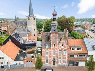 Achter deze monumentale gevel schuilt een herenwoning die haar geschiedenis moeiteloos combineert met een verrassende hoeveelheid leefruimte. Het herenhuis, ontworpen door architect Edward Careels, opgetrokken in <strong>neo-Vlaamserenaissancestijl en gedateerd 1892, </strong>werd als beschermd monument erkend om zijn artistieke waarde en onderscheidt zich door zijn uitgesproken architectuur, royale vertrekken en karaktervolle details. Achteraan vormt de bijzonder groene tuin met zwembad een onverwacht rustig decor bij dit statige geheel.<br /><br />De ligging in het hart van Zandhoven maakt het plaatje compleet: winkels, bakker, horeca, openbaar vervoer en dagelijkse voorzieningen bevinden zich op korte afstand, waardoor heel wat verplaatsingen eenvoudig te voet of met de fiets kunnen. Tegelijk zorgen de nabijgelegen E313 en E34 voor een vlotte verbinding richting Antwerpen en de omliggende gemeenten. Zo combineert deze locatie het gemak van wonen in het dorpscentrum met een bijzonder aangename private buitenruimte achter de woning.<br /><br /><strong>Indeling</strong><br />De statige inkomhal vormt het centrale vertrekpunt van de woning en geeft toegang tot de verschillende leefruimtes. Aan de straatzijde bevindt zich de bijzonder royale woonkamer met eetruimte, die achteraan verderloopt naar de lichtrijke veranda en zo een mooie verbinding maakt met de tuin.<br />Verder beschikt het gelijkvloers over een afzonderlijke eetkamer aansluitend de keuken en wasplaats, maar ook over een bureau met aanpalend archief. Die extra vertrekken maken de woning bijzonder interessant voor wie wonen en werken onder één dak wil combineren. Via een hall bereikt u bovendien een ruime hobbyruimte/extra bureel, de technische ruimte van het zwembad en de inpandige garage.<br /><br />De tuin vormt zonder twijfel één van de verrassingen van deze woning. Achter de historische gevel ontvouwt zich een verzorgde, groene buitenruimte met ruime terrassen, pergola en zwembad, omgeven door volwassen beplanting die voor een aangename besloten sfeer zorgt. Een automatische poort achteraan het perceel biedt rechtstreeks toegang tot de tuin en zorgt voor extra praktisch gemak.<br /><br />Op de <strong>eerste verdieping</strong> bevinden zich 3 volwaardige slaapkamers, een dressing en twee badkamers.<br /><br />De <strong>tweede en derde verdieping vormen samen een bijzonder ruim duplexgedeelte</strong> met een grote woonkamer, eigen keuken en badkamer, een karaktervolle torenkamer en op het bovenste niveau nog een slaapkamer. Hierdoor ontstaat een bijna zelfstandige woonverdieping die zich uitstekend leent als gastenverblijf, thuiskantoor of eigen plek voor opgroeiende kinderen en tieners.<br />Ook aan bergruimte ontbreekt het niet: de woning beschikt over een ruime wijnkelder en tal van bijkomende functionele ruimtes.<br /><br /><strong>Bijzonderheden</strong><br />Met haar 20 zonnepanelen, uitzonderlijke oppervlakte, vier slaapkamers, verschillende leef- en werkruimtes, inpandige garage, zwembad en afzonderlijk bruikbaar duplexgedeelte biedt deze woning een flexibiliteit die zelden voorkomt. Vooral de combinatie van de historische gevel, de besloten groene tuin en de verrassend veelzijdige indeling maakt het geheel bijzonder.