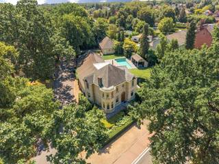 Deze prachtige, ruime villa is gelegen op een mooi aangelegd perceel met een uitzonderlijk gevoel van rust en privacy. De woning combineert royale leefruimten met een praktische indeling en tal van extra's, waaronder een buitenzwembad, een sfeervolle buitenkeuken met bar, een cinemaruimte en een indrukwekkende vrijstaande garage met plaats voor vier wagens. De fraai aangelegde tuin vormt een oase van groen.<br /><br />De woning omvat op het gelijkvloers een inkomhal, een ruime leefruimte bestaande uit een zithoek met houtkachel, eetkamer en gezellige tv-/leeshoek, een veranda met uitzicht op de tuin, een volledig ingerichte keuken, een bijkeuken/wasplaats, een ingerichte badkamer met dressing, een multifunctionele bar met buitenkeuken en verdieping met opslagruimte en cinemazaal, een dubbele inpandige garage en een kelder.<br /><br />Op de eerste verdieping bevinden zich vier volwaardige slaapkamers, een ingerichte douchekamer en een praktische bergzolder, bereikbaar via vast trap (met valluik).<br /><br />De prachtige tuin is voorzien van een buitenzwembad met een ruim overdekt terras en een voorziening voor een berging of kleedruimte. Daarnaast beschikt het eigendom over een vrijstaande garage met plaats voor vier wagens en een tuinhuis.<br /><br />Een uniek geheel met tal van mogelijkheden, afgewerkt met oog voor comfort en gelegen in een bijzonder groene en private omgeving.<br /><br />Indeling<br />Gelijkvloers<br />Via de inkomhal met gastentoilet en vestiaire en trap naar de eerste verdieping betreedt u deze ruime woning. De royale leefruimte is speels ingedeeld dankzij enkele niveauverschillen, waardoor een aangename en karaktervolle sfeer ontstaat. De zithoek met houtkachel vormt het gezellige hart van de woning en sluit mooi aan op de eetkamer en de afzonderlijke tv-/leeshoek.<br /><br />Aansluitend bevindt zich de lichtrijke veranda, waar u het hele jaar door kunt genieten van een prachtig uitzicht over de fraai aangelegde tuin.<br /><br />De volledig ingerichte keuken (combi-oven, heteluchtoven, koelkast, vaatwasser, inductiekookplaat, dampkap en grillplaat) biedt alle nodige comfort. Via de achteringang komt u in een sas dewelke toegang biedt tot de praktische bijkeuken/wasplaats, de ingerichte badkamer met aansluitend dressing en de keuken.<br /><br />Een absolute meerwaarde is de gezellige bar met buitenkeuken. Via een vaste trap bereikt u de verdieping boven deze ruimte, waar zich een praktische opslagruimte en een sfeervolle cinemazaal bevinden.<br /><br />Verder beschikt het gelijkvloers over een dubbele inpandige garage en een kelder die extra bergruimte biedt.<br /><br />Eerste verdieping<br />Via de trap in de inkomhal bereikt u de overloop, die toegang verleent tot vier ruime slaapkamers en een douchekamer (wastafel, douche en toilet).<br /><br />Via een vaste trap (met valluik) bereikt u bovendien de praktische opbergzolder.<br /><br />Kelder<br />De woning beschikt over een praktische kelder die dienst doet als extra opslagruimte.<br /><br />Tuin<br />De prachtig aangelegde tuin biedt optimale privacy en vormt een heerlijke plek om tot rust te komen. Het buitenzwembad vormt samen met het ruime overdekte terras het perfecte decor om te genieten van warme zomerdagen. Bij het zwembad zijn tevens voorzieningen aanwezig voor een berging en/of kleedruimte.<br /><br />Verder bevindt zich achteraan het perceel een ruime vrijstaande garage met plaats voor vier wagens. Daarnaast is er nog een afzonderlijk tuinhuis aanwezig.<br /><br />Bijzonderheden<br />•Zeer ruime villa met speelse indeling <br />•Hoogwaardige afwerking<br />•Alarm<br />•Camerabewaking (5 camera’s aanwezig)<br />•Volledig omheind en afgesloten perceel<br />•Airco aanwezig (veranda en hoofdslaapkamer)<br />•Buitenzwembad (4,5 x 11m)<br />•Vrijstaande garage van ca. 90 m²<br />•Verwarming op aardgas<br />•Zuidwest georiënteerde tuin