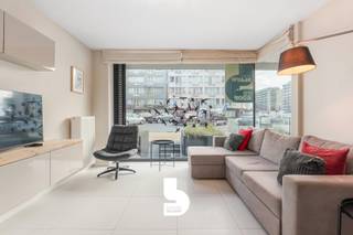 Op amper 30 meter van de zeedijk bevindt zich dit moderne en lichtrijke gelijkvloerse appartement met zijdelings zeezicht, twee slaapkamers en een exclusief zonneterras van maar liefst 28 m². De recente residentie onderscheidt zich door haar eigentijdse architectuur en biedt dankzij slechts één appartement per verdieping een extra gevoel van rust en privacy.<br /><br />Het appartement is stijlvol en luxueus ingericht, met bijzondere aandacht voor een optimaal ruimtegebruik. De praktische inbouwkasten, waaronder een opklapbaar bed, zorgen voor extra comfort en opbergruimte. Met twee slaapkamers biedt het appartement plaats aan vier personen, waardoor het ideaal is als tweede verblijf aan zee of als comfortabele eigen woonst.<br /><br />Een absolute troef is het ruime, volledig afgesloten zonneterras van 28 m², rechtstreeks toegankelijk vanuit het appartement en ideaal om in alle privacy van de zon te genieten. Dankzij de ligging op het gelijkvloers is het appartement bovendien bijzonder vlot toegankelijk.<br /><br />De residentie beschikt over een ruime lift die conform is aan de geldende normen. Daarnaast zijn er een gemeenschappelijke fietsenberging en extra bergruimte, zowel in het appartement zelf als in de kelder.<br /><br />De ligging is bijzonder gunstig: op wandelafstand vind je het openbaar vervoer, restaurants, winkels, het warenhuis, het nieuwe stedelijke zwembad en diverse sportfaciliteiten, waaronder golf, voetbal en basketbal.<br /><br />Tot slot beschikt het appartement over een blanco elektrische keuring.