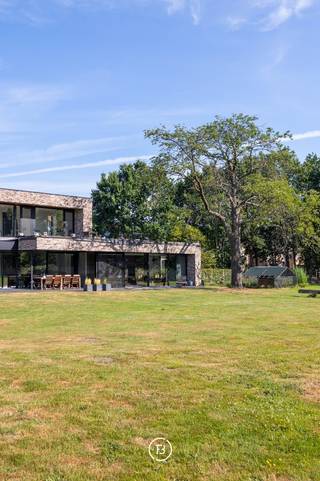 Deze stijlvolle, moderne villa uit 2018 is gelegen op een uitzonderlijk breed perceel van maar liefst 5.016 m² en biedt een unieke combinatie van hedendaags wooncomfort, privacy en een groene, landelijke omgeving. De tijdloze architectuur, gekenmerkt door grote raampartijen, zorgt voor een overvloed aan natuurlijk licht en creëert een harmonieuze verbinding tussen binnen en buiten.<br /><br />Het royale perceel vormt een absolute meerwaarde voor wie houdt van ruimte en natuur. Dankzij de omvang en de rustige ligging biedt het tal van mogelijkheden voor dierenliefhebbers en paardenliefhebbers, met voldoende plaats om dieren aan huis te houden of het terrein naar eigen wens in te richten.<br /><br />Ook voor wie wonen en werken wil combineren, is deze woning bijzonder geschikt. Er zijn twee afzonderlijke ruimtes voorzien die perfect kunnen dienen als praktijk, bureau of kantoor aan huis.<br /><br />De leefruimte werd ontworpen met oog voor openheid, licht en wooncomfort. De volledig uitgeruste keuken is voorzien van hoogwaardige Gaggenau-toestellen en een Quooker-kraan. Vanuit de keuken en de aangrenzende leefruimte geniet u van een prachtig, weids uitzicht over de zuidoost georiënteerde tuin en de achterliggende natuur, waardoor elk seizoen optimaal beleefd kan worden.<br /><br />Aansluitend aan de keuken bevindt zich een ruime berging die eveneens rechtstreeks bereikbaar is via de carport. Daarnaast beschikt de woning over talrijke maatkasten, een tweede grote berging en een aparte wasruimte met douche, waardoor functionaliteit en opbergruimte ruimschoots aanwezig zijn.<br /><br />Het wooncomfort wordt verder versterkt door een uitgebreid domoticasysteem, camerabewaking, een alarmsysteem en een geïntegreerde muziekinstallatie die doorheen de volledige woning voor extra gebruiksgemak en sfeer zorgen.<br /><br />De villa telt vijf volwaardige slaapkamers en twee stijlvolle badkamers. De master bedroom beschikt over een ensuite badkamer en een ruime dressing, met een rustgevend uitzicht op het omliggende groen.<br /><br />Ook op technisch vlak voldoet deze woning aan de hoogste verwachtingen. Dankzij het gunstige energielabel A en de conforme elektrische installatie is deze villa volledig klaar voor de toekomst.<br /><br />Deze uitzonderlijke eigendom biedt een zeldzame combinatie van moderne architectuur, hoogwaardig wooncomfort, een prachtig natuurzicht en een royaal perceel met tal van mogelijkheden voor gezinnen, zelfstandigen én dieren- of paardenliefhebbers.