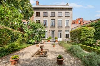 Achter deze statige gevel schuilt een uitzonderlijke herenwoning met een bewoonbare oppervlakte van maar liefst 546 m². Authentieke elementen werden doorheen de woning met zorg bewaard en versterken het unieke karakter van deze eigendom. De royale volumes, dubbele toegang en flexibele indeling maken deze eigendom uitermate geschikt voor wie op zoek is naar een ruime gezinswoning, een combinatie van wonen en werken of een eigendom met uiteenlopende gebruiksmogelijkheden.<br /><br />De woning maakt deel uit van het beschermde stadsgezicht ‘Vredeberg’ en is opgenomen als bouwkundig erfgoed. Hierdoor is de residentiële renovatieverplichting niet van toepassing.<br /><br />Via de centrale inkomhal bereikt u de bureau- of praktijkruimte, de ruime eetkamer en de lichtrijke leefruimte met een prachtig groen zicht op de privatieve tuin van 185m². De afzonderlijke keuken biedt alle ruimte en comfort voor dagelijks gebruik. Op het gelijkvloers bevinden zich verder een slaapkamer of polyvalente ruimte met ingemaakte kasten, een gastentoilet, berging, wasruimte, toegang tot de droge kelder en een bijkomende binnenplaats van 25m².<br /><br />De onderhoudsvriendelijke mediterrane tuin vormt een rustige buitenruimte en geeft rechtstreeks toegang tot de dubbele garage met elektrische poort en extra opbergruimte, bereikbaar via het Vlietje.<br /> <br />De eerste verdieping is bereikbaar via de statige trappenhal of comfortabel met de lift, die eveneens toegankelijk is via de tweede inkomdeur. Hier bevinden zich vier volwaardige slaapkamers, waarvan één met een ensuite badkamer voorzien van douche, bidet en dubbel lavabomeubel. Daarnaast is er een tweede badkamer met ligbad, toilet en lavabomeubel.<br /> <br />Een absolute troef is de voormalige tandartspraktijk op de tweede verdieping. Met een oppervlakte van maar liefst 177 m² biedt deze verdieping uitzonderlijk veel potentieel voor extra woonruimte, een praktijk, atelier of een andere invulling. Aansluitend bevinden zich nog twee ruime zolderverdiepingen, die bijkomende mogelijkheden bieden.