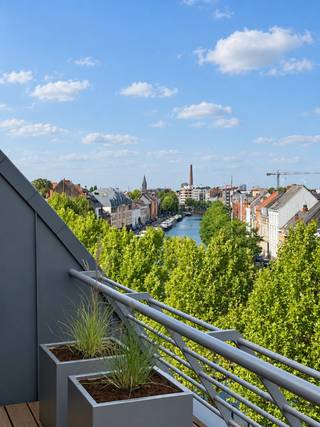 TE KOOP – GENT. Op een bijzonder gegeerde locatie aan de Visserij geniet u van een unieke woonbeleving met een totale oppervlakte van maar liefst 230 m² en circa 100 m² aan royale terrassen. Het adembenemende 180°-uitzicht over het water en de groene omgeving vormt hier elke dag opnieuw het decor.<br />De verschillende terrassen nodigen uit om volop van het buitenleven te genieten: van een rustig ontbijt in de ochtendzon tot een aperitief of lange zomeravond met familie en vrienden.<br />Ook binnen voelt u zich meteen thuis. De massief houten parketvloer, natuurlijke materialen en kwalitatieve afwerking creëren een warme, stijlvolle sfeer. Grote raampartijen halen het landschap naar binnen en verbinden de leefruimtes naadloos met de terrassen.<br />De inkomhal met ingemaakte vestiairekast biedt toegang tot het gastentoilet, een eerste badkamer en een ruime slaapkamer, momenteel ingericht als bureau. Vervolgens ontvouwt zich de royale leefruimte met volledig uitgeruste open keuken, hoogwaardige toestellen, een centraal kookeiland en een geïntegreerde wijnkoeler: de ideale plek om samen te koken, te aperitieven en uitgebreid te tafelen.<br />Via de elegante houten draaitrap bereikt u de bovenverdieping en het ruime zonneterras, waar u in alle privacy van het panoramische uitzicht geniet. Hier bevinden zich twee volwaardige slaapkamers, een stijlvolle badkamer, een aparte dressing en een praktische wasruimte met wasmachine en droogkast.<br />Talrijke ingemaakte kasten, doordachte opbergoplossingen en meerdere buitenbergingen bieden uitzonderlijk veel comfort zonder afbreuk te doen aan het ruimtelijke gevoel.<br />Een zeldzaam penthouse waar royale volumes, hoogwaardige afwerking en uitzonderlijk buitenleven samenkomen op een unieke ligging aan de Visserij.<br />Mogelijkheid tot aankoop autostaanplaats in het gebouw.
