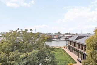In een levendige buurt, op wandelafstand van het water en met een vlotte verbinding naar het stadscentrum en het openbaar vervoer, bevindt zich dit karaktervolle triplexappartement in een kleinschalige residentie.<br />Met een bewoonbare oppervlakte van maar liefst 150 m², een zonnig dakterras en een bijzonder uitzicht op het water combineert deze woning ruimte, licht en authenticiteit.<br /><br />Via de inkomhal met gastentoilet kom je in een lichtrijke leefruimte waar hoge plafonds, royale raampartijen en een open indeling zorgen voor een aangenaam gevoel van ruimte. <br /><br />De ruime leefruimte met zit- en eetgedeelte sluit naadloos aan op de open keuken en geniet van een prachtig uitzicht over het water. Authentieke elementen van de voormalige loodsen werden met zorg behouden en geven het geheel een uitgesproken karakter.<br /><br />Op de eerste verdieping bevindt zich de ruime masterbedroom, die eveneens geniet van een schitterend uitzicht op het water. De ensuite badkamer is uitgerust met een ligbad, een douche, een dubbele lavabo en een toilet.<br />De bovenste verdieping biedt een tweede comfortabele slaapkamer met rechtstreekse toegang tot het zonnige dakterras waar u in alle rust kunt genieten van de buitenruimte.<br /><br />Een appartement met een eigen identiteit, waar ruimte, licht en authentieke details samenkomen. Ideaal voor wie op zoek is naar een bijzondere woonplek met een flexibele indeling en connectie met het water.<br /><br />Extra troef: de mogelijkheid om een ondergrondse parkeerplaats te huren of aan te kopen.