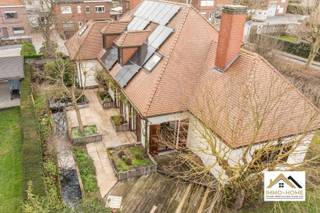Deze stijlvolle villa bevindt zich in het groene Merelbeke. Je komt binnen via een ruime, elegante traphal die toegang biedt tot alle vertrekken op het gelijkvloers. Aan de voorzijde bevindt zich een zeer ruim bureau, ideaal voor thuiswerk of praktijkruimte. Verder is er een apart gastentoilet en een vlotte doorgang naar de leefruimtes. De volledig ingerichte keuken is uitgerust met een grote eethoek en kamerhoge ramen die zorgen voor overvloedig daglicht en een directe verbinding met de tuin. Aansluitend bevindt zich een praktische bijkeuken met ruimte voor wasmachines en extra opslag. Daarnaast is er een dubbele garage met automatische poorten, geschikt voor twee wagens en bijkomende bergruimte. De leefruimte is royaal en omvat een eetplaats met zicht op de tuin. Uniek aan deze woning is de gezellige open haardkamer met hoog plafond, die warmte en sfeer toevoegt aan het geheel. Bovendien is er een kelderruimte aanwezig, handig als extra opslag. Op de bovenverdieping leidt een stijlvolle nachthal naar vier ruime slaapkamers. De master bedroom beschikt over een comfortabele dressing met daglicht. Twee slaapkamers bieden ruim plaats aan een bed en kasten, terwijl de vierde kamer bijzonder groot is en tal van inrichtingsmogelijkheden biedt. Ook een nachttoilet is voorzien op deze verdieping. De tuin, momenteel in winterslaap, is een ware oase voor liefhebbers van groen. Dankzij de verzorgde mixborders, een sfeervolle vijver en het beschutte terras is het hier aangenaam vertoeven. Als extra troef is er in de hoek van de tuin een charmante blokhut met sauna. Deze villa combineert comfort met klasse: zonnepanelen, een ruime oprit en een luxueuze uitstraling maken het geheel compleet. Ideaal voor wie op zoek is naar een ruime, instapklare woning met karakter, privacy en hoogwaardige afwerking, in een rustige en toch vlot bereikbare omgeving. Bezoekdag: 16/05. Inschrijven via mail naar tommy@immo-home.be, geen telefonische inschrijvingen! Volg ons op Fb en Insta. Voor meer info: www.immo-home.be. GRATIS SCHATTING &amp; GRATIS FINANCIEEL ADVIES