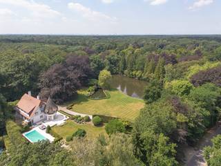 <p><strong>Villa De Maretak – Een stukje geschiedenis in Kapellenbos</strong></p>
<p>Gebouwd in 1911 naar een ontwerp van architect Florent Van Reeth<strong>,</strong> werd Villa De Maretak opgetrokken als buitenverblijf voor de Antwerpse familie Muls. De naam verwijst naar hun stadsvilla "De Maretak" aan het Vleminckveld. Latere renovaties hebben bijgedragen aan het behoud van die rijke geschiedenis en de uitstraling van weleer.</p>
<p>Op een prachtig aangelegd perceel van 16.629 m² vormt deze karaktervolle villa een ware blikvanger. De authentieke architectuur, met de kenmerkende rieten toren, verleent de woning een unieke en tijdloze uitstraling. Rondom geniet u van een volgroeide tuin, een zwembad en een uitzonderlijke ligging aan het water. Een zeldzaam eigendom waar historische charme, ruimte en natuur op een vanzelfsprekende manier samenkomen.De woning verwelkomt u in een royale inkomhal met vide, natuurstenen vloer en een elegante trap die meteen de toon zet. Van hieruit vloeien de leefruimtes op een natuurlijke manier in elkaar over. De salon, met zijn warme parketvloer, houten balkenplafond en open haard, vormt het hart van de woning en geniet dankzij de grote raampartijen van een permanente relatie met de tuin. Aansluitend bevindt zich een tweede leefruimte die zich perfect leent als tv-kamer of familiekamer.</p>
<p>De eetkamer, ondergebracht in de karaktervolle ronde toren, biedt rondom een prachtig uitzicht op het omliggende groen en sluit rechtstreeks aan op de terrassen. De afzonderlijke leefkeuken is praktisch ingericht, geniet van veel natuurlijk licht en vormt een aangename plek voor dagelijks gebruik.</p>
<p>De eerste verdieping werd ingericht met het oog op comfort voor het hele gezin. De masterbedroom, ondergebracht in de karaktervolle toren van de woning, vormt het absolute middelpunt. Dankzij de royale oppervlakte, het ronde grondplan en de ensuite badkamer krijgt deze kamer een heel eigen uitstraling. Verder bevinden zich op deze verdieping nog twee ruime slaapkamers, elk voorzien van een eigen badkamer en rechtstreekse toegang tot een balkon met uitzicht op de tuin. Een doordachte indeling die elke slaapkamer haar eigen comfort en privacy geeft, zonder het familiale karakter van de woning te verliezen.</p>
<p>De woning beschikt ook over een ruime kelder, momenteel ingericht als thuisbioscoop en voorzien van de technische ruimtes.</p>
<p>De zolderverdieping is reeds voorzien van een vierde badkamer en biedt nog de mogelijkheid om twee extra slaapkamers te realiseren. Daarnaast leent deze verdieping zich ook perfect als hobbyruimte, kinderverdieping of thuiskantoor.</p>
<p>De tuin vormt zonder twijfel één van de absolute troeven van dit eigendom. Een doordacht landschapsontwerp combineert perfect onderhouden hagen, volwassen bomen, royale gazons en meerdere terrassen tot een buitenruimte die elk seizoen tot haar recht komt. De verschillende terrassen nodigen uit om op elk moment van de dag te genieten van zon, schaduw en het omliggende groen.</p>
<p>Het perceel strekt zich uit tot aan een idyllische vijver, die de tuin een uitzonderlijke diepte en een parkachtige uitstraling verleent. De garages, ruime oprit met rotonde en zorgvuldig aangelegde buitenruimtes maken het geheel compleet. Een omgeving waar rust, privacy en natuur naadloos samenkomen.<br /><br /></p>
<p>Deze villa combineert de rust van Kapellenbos met een uitstekende bereikbaarheid. De centra van Kapellen en Heide, met hun winkels, scholen en restaurants, bevinden zich op korte afstand. Ook het station van Heide en de belangrijkste verbindingswegen liggen vlakbij, waardoor u geniet van een vlotte verbinding richting Antwerpen, Brussel en Nederland.</p>