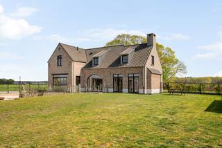 Deze stijlvolle woning is gebouwd in 2020 en is afgewerkt met kwalitatieve en duurzame materialen. Deze eigendom beschikt over een sfeervolle woonkamer, lichte leefkeuken, wasplaats, 4 slaapkamers op de 1e verdieping, bureau of 5e slaapkamer op de gelijkvloerse verdieping, badkamer, 2e nog af te werken badkamer, dressing en dubbele carport met overdekt terras. <br />De villa is gelegen op een groen domein met vrij uitzicht op omliggende weilanden. Hier geniet u van ruimte en rust op een interessante locatie vlakbij de Nederlandse grens. <br /><br />Gelijkvloers:<br />U betreedt de woning via de ruime inkomhal met apart toilet. Hierlangs heeft u toegang tot de sfeervolle woonkamer op tegelparket dat via de grote ramen achteraan uitzicht geeft op de open tuin. De moderne leefkeuken met groot eiland en natuurstenen werkblad is voorzien van kwalitatieve toestellen (inductievuur, combi oven/micro, oven, warmhoudlade, vaatwasmachine, koelkast). De wasplaats is toegankelijk via een ingewerkte deur in de keuken wat voor een strak geheel zorgt. Vooraan de woning bevindt er zich nog een bureauruimte of extra gelijkvloerse slaapkamer afgewerkt met een prachtige visgraatparkettegel.<br /><br />Eerste verdieping:<br />De bovenverdieping is eveneens uitgerust met parket en is opgedeeld in 4 slaapkamers waarvan de masterbedroom voorzien is van een dressing en eigen badkamer. Verder bevindt er zich nog een afzonderlijk toilet en tweede badkamer die nog verder naar eigen smaak af te werken is. <br /><br />Tuin:<br />In de tuin is het aangenaam vertoeven door het weidse uitzicht. De tuin is voorzien van een ruim bijgebouw waar plaats is voor meerdere wagens en ook gebruikt kan worden als overdekt terras. Doordat het perceel ca. 6.886m² is, bestaat de mogelijkheid dieren te houden.<br /><br />Bijzonderheden:<br />- Ruim perceel met open zichten<br />- Instaklare woning met kwalitatieve afwerking<br />- Regenwaterput aangesloten op toiletten en wasmachine <br />- 2 geboorde grondwaterputten van 12m diepte<br />- Energiezuinige woning (E30) met zonnepanelen en vloerverwarming <br />- Alarm en domotica