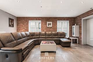 Voor meer info en foto’s, surf naar www.swevers.be – Deze ruime open bebouwing in Nieuwerkerken biedt met een bewoonbare oppervlakte van 239 m² alle comfort voor een groot gezin. De woning werd gebouwd in 1996 en ligt op een zuidgericht perceel van 8 are aan de Wouterveld 56. Via de inkomhal met gastentoilet bereikt u de lichtrijke leefruimte, waar zithoek, eetkamer en keuken mooi in elkaar overlopen. De keuken beschikt over voldoende werk- en bergruimte voor dagelijks gebruik. Op het gelijkvloers bevindt zich bovendien een ruime slaapkamer en een badkamer met ligbad en enkele wastafel. De eerste verdieping telt vier volwaardige slaapkamers van respectievelijk 18 m², 16 m², 16 m² en 16 m². Daarnaast is er een tweede badkamer met inloopdouche, toilet en een dubbele wastafel. De ruime open zolderverdieping op de tweede verdieping biedt tal van mogelijkheden als extra slaapkamer, hobbyruimte of extra opslagplaats. Ook praktisch scoort deze woning sterk dankzij de garage van 23 m² . Doorheen de jaren werd de woning zorgvuldig onderhouden en op verschillende vlakken vernieuwd. Daarnaast werden in 2018 zonnepanelen geplaatst, wat bijdraagt aan een lagere energiefactuur. Recente investeringen omvatten de plaatsing van een warmtepomp en een gaskachel in 2023, wat zorgt voor extra comfort en een efficiënte verwarming van de woning. Buiten geniet u van een zonnige, zuidgerichte tuin waar kinderen kunnen spelen en waar u optimaal kan genieten van lange zomeravonden. De ligging is bovendien bijzonder gunstig, met scholen en kinderopvang op wandelafstand, een bushalte op slechts 150 meter, winkels en ontspanningsmogelijkheden in de buurt en een vlotte verbinding naar het station en de autosnelweg. Bent u op zoek naar een ruime gezinswoning met vijf slaapkamers, twee badkamers, zonnepanelen en een zonnig perceel in Nieuwerkerken? Dan is deze woning zeker een bezoek waard. Voor meer informatie, bel 012 699 900. Bron bewoonbare oppervlakte: EPC – verslag