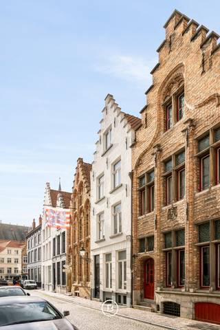 This elegant townhouse, fully renovated in 2018, seamlessly combines timeless elegance with modern living comfort. It features a unique Japanese-inspired city garden with a covered water terrace, offering an exceptional living experience in the heart of Bruges' prestigious "Golden Triangle."<br /><br />Layout<br />Ground floor:<br />Upon entering, you are welcomed by a spacious entrance hall with a cloakroom and guest toilet. The bright living area boasts high-quality parquet flooring and a modern gas fireplace. A centrally located patio enhances natural light and creates a subtle separation from the fully equipped kitchen, which includes a generous dining area and offers a stunning view of the serene city garden.<br /><br />Basement level:<br />An open staircase leads to a stylishly designed living space (Cave) with underfloor heating and authentic vaulted ceilings, directly connected to the exclusive covered water terrace. This level also includes a guest toilet, a spacious storage room, a laundry room, and a practical bicycle storage area.<br /><br />First floor:<br />This floor comprises two spacious bedrooms, one of which features a dressing room. Each bedroom has its own fully equipped bathroom. Additionally, there is a separate toilet and a night hall with built-in wardrobes.<br /><br />Second floor:<br />The top floor is accessible via two separate staircases. At the rear, one staircase leads to a comfortable guest room, while at the front, a second staircase opens onto a spacious and charming bedroom with a mezzanine, as well as an open office space with built-in wardrobes.<br /><br />Key Features<br />✔ Fully renovated in 2018<br />✔ Living area: 374 m²<br />✔ Prime location in Bruges' "Golden Triangle"<br />✔ Energy-efficient (EPC label B)<br />✔ Bright and spacious living areas