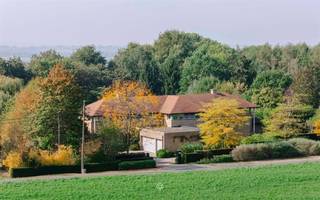 <h1><span>Architecturale villa met zwembad op uitzonderlijk privédomein in de Vlaamse Ardennen</span></h1><p><span>VLAAMSE ARDENNEN</span><span> Sommige woningen imponeren door hun grandeur, andere door de rust die ze uitstralen. Hier komen beide op uitzonderlijke wijze samen.</span></p><p><span>Discreet verscholen in het groen van de Vlaamse Ardennen bevindt zich een bijzonder architecturaal eigendom waar ruimte, privacy en verfijning centraal staan. Op een zuidgericht domein van maar liefst 70a90ca ontvouwt zich een statige villa met circa 650 m² bewoonbare oppervlakte, ontworpen volgens een uitgesproken horizontale en symmetrische architectuur.</span></p><p><span>Wat zich aan de straatzijde eerder ingetogen presenteert, onthult eenmaal binnen zijn ware grandeur. Royale leefvolumes, indrukwekkende zichtlijnen en grote raampartijen creëren een uitzonderlijk gevoel van ruimte en licht. De woning opent zich volledig naar een prachtig aangelegd privépark, waar slingerende paden, strak geschoren hagen, volwassen bomen en drie vijvers een harmonieus geheel vormen. Centraal in dit groene decor ligt het verwarmde zwembad van 6 x 11 meter, afgewerkt in glasmozaïek.</span></p><p><span>Ook binnen weerspiegelt elk detail de kwaliteit van het eigendom. Massief parket, Portugese witsteen, marmer, natuursteen en verfijnd maatwerk zorgen voor een tijdloze elegantie. De royale leefruimte met stijlvolle doorkijkhaard vormt het hart van de woning en sluit aan op een afzonderlijke eetkamer en een bijzonder ruime, hoogwaardig uitgeruste Vossaert-leefkeuken. Een wintertuin, gezellige TV- en speelkamer en talrijke discreet geïntegreerde praktische ruimtes vervolledigen het gelijkvloers.</span></p><p><span>Een bijzondere troef is de volledig afzonderlijk toegankelijke praktijkvleugel, waardoor wonen en werken hier moeiteloos samengaan zonder aan privacy in te boeten. Ideaal voor een vrij beroep, kantoor of praktijk aan huis.</span></p><p><span>Twee afzonderlijke trappen leiden naar de verdieping, waar de symmetrische indeling zich vertaalt in een kinder- en oudervleugel. De indrukwekkende parental suite omvat een royale slaapkamer, twee dressings en een luxueuze badkamer met whirlpoolbad en Finse sauna. Daarnaast beschikt de woning over drie ruime slaapkamers, bijkomende badkamers en een royale fitness- of hobbyruimte.</span></p><p><span>Ook op het vlak van comfort en techniek werd aan vrijwel alles gedacht: 20 zonnepanelen, airconditioning, geïntegreerde Bang &amp; Olufsen-audio, uitgebreide beveiliging, centraal stofzuigsysteem, zonwering en een regenwaterreservoir van 30.000 liter. Een professioneel ingerichte wijnkelder, diverse kelderruimtes en een inpandige garage voor drie wagens onderstrepen het uitzonderlijke karakter van dit eigendom.</span></p><p><span>Maar de ware luxe laat zich hier niet uitsluitend in cijfers of materialen vatten. Ze schuilt in de rust van het park, het licht dat door de woning stroomt, de harmonie tussen architectuur en landschap en het zeldzame gevoel van afzondering.</span></p><p><span>Een exclusief eigendom waar grandeur en discretie elkaar ontmoeten, en waar wonen, werken en ontspannen in volmaakte harmonie samenkomen.</span></p><p><span>Prijs en volledig adres op aanvraag.</span></p>