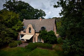 Op een bijzonder mooie en rustige locatie in het residentiële Schotenhof bevindt zich deze karaktervolle familievilla, omgeven door een volwassen tuin en genietend van een uitzonderlijke privacy.<br /><br />De eigendom combineert een royaal woonvolume met een warme, tijdloze uitstraling en een sterke verbondenheid met de tuin. Dankzij de uitstekende zuidoriëntatie, de verschillende leefruimtes en het charmante eiken bijgebouw is dit bovenal een huis waar binnen- en buitenleven op een vanzelfsprekende manier in elkaar overvloeien.<br /><br />Ook de ligging is bijzonder aangenaam: discreet en groen, maar tegelijk op korte afstand van zowel Schoten als ’s-Gravenwezel, met scholen, winkels en gerenommeerde sportclubs in de onmiddellijke omgeving.<br /><br />Een huis met ruimte en karakter<br /><br />De woning wordt benaderd via een royale voortuin met sfeervolle waterpartij. Enkele treden leiden naar de brede inkomdeur en de ruime ontvangsthal, van waaruit dubbele glazen deuren meteen een mooie doorkijk bieden naar de leefvertrekken en het groen rondom.<br /><br />De natuurstenen vloer loopt harmonieus door naar de verschillende leefruimtes. Het iets hoger gelegen salon met open haard vormt een intieme en sfeervolle plek, terwijl het aansluitende eetgedeelte zich naar de tuin richt. Grote raampartijen aan zowel voor- als achterzijde zorgen doorheen de woning voor veel natuurlijk licht en een voortdurend contact met de omgeving.<br /><br />Centraal in het dagelijkse leven staat de ruime leefkeuken. De karaktervolle AGA vormt er het hart van de ruimte, aangevuld met Miele-inbouwapparatuur en een royaal eiland waaraan ook informeel kan worden gegeten. Een glazen deur opent rechtstreeks naar het terras en de zuidgerichte tuin.<br /><br />Aansluitend bevindt zich een afzonderlijke kamer die zich uitstekend leent als bureau, bibliotheek of polyvalente ruimte en eveneens toegang biedt tot het terras. Een ruime bijkeuken zorgt voor het nodige praktische comfort.<br /><br />De dubbele inpandige garage biedt plaats aan twee wagens en beschikt over bijkomende bergruimte.<br /><br />Privévertrekken<br /><br />Op de eerste verdieping bevinden zich de hoofdslaapkamer en drie bijkomende slaapkamers, samen met twee badkamers. Talrijke ingemaakte kasten zorgen voor een bijzonder praktische indeling.<br /><br />Een afzonderlijke trap leidt verder naar een verrassend royale bovenverdieping met mezzanine. Een ruimte die zich naar eigen behoefte laat invullen als bijkomende slaapkamer, gastenverblijf, hobbyruimte of thuisbureau. Ook de zolder is vanaf hier bereikbaar.<br /><br />De woning beschikt bovendien over een zeer ruime kelderverdieping, waardoor ook aan berging en technische ruimte geen gebrek is.<br /><br />Een tuin in alle privacy<br /><br />De volwassen tuin vormt een essentieel onderdeel van de beleving van deze eigendom. De zuidelijke oriëntatie, het vele groen en de afwezigheid van inkijk creëren een bijzonder aangename en besloten sfeer.<br /><br />Een mooi uitgevoerd eiken bijgebouw, voorzien van verwarming en bergruimte, geeft de tuin nog een extra dimensie en biedt mogelijkheden voor wie op zoek is naar een afzonderlijke werk-, hobby- of ontspanningsruimte.<br /><br />Een eigendom die niet zozeer overtuigt door één afzonderlijk element, maar door het geheel: ruimte, privacy, groen en een bijzonder aangename woonkwaliteit op één van de meest gegeerde residentiële locaties van Schoten.<br /><br />Bijzonderheden<br /><br />• Residentieel en discreet gelegen in Schotenhof<br />• Op korte afstand van Schoten en ’s-Gravenwezel<br />• Royale familievilla met vijf mogelijke slaapkamers<br />• Twee badkamers<br />• Ruime leefkeuken met AGA<br />• Zuidgerichte tuin met uitzonderlijke privacy<br />• Verwarmd eiken bijgebouw<br />• Dubbele inpandige garage en bijkomende garage<br />• Royale kelder- en bergruimtes<br />• Nabij scholen, winkels en gerenommeerde sportfaciliteiten