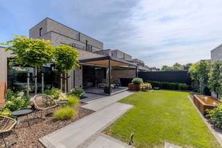 <p><strong>Instapklaar gelijkvloers appartement met carport, berging, luxe afwerking en aangelegde tuin</strong></p>
<p>Dit <strong>gelijkvloers appartement</strong> is een echte parel voor wie houdt van comfort, privacy en een hoogwaardige afwerking. Het appartement beschikt over een <strong>overdekte carport/staanplaats</strong>, een praktische <strong>berging</strong> en een volledig aangelegde tuin met overdekt terras.</p>
<p>Bij het betreden van het appartement kom je binnen in de <strong>inkomhal met gastentoilet</strong>. Van hieruit heb je toegang tot de ruime leefruimte, die stijlvol is opgedeeld in een gezellige zithoek en een volledig ingerichte eetkeuken. De leefruimte is afgewerkt met een mooie <strong>parketvloer</strong> en straalt dankzij de kwalitatieve materialen meteen warmte en klasse uit.</p>
<p>De zithoek is voorzien van een sfeervolle <strong>ethanolhaard</strong>, ideaal voor gezellige avonden. Daarnaast werd er ook gedacht aan modern wooncomfort: de <strong>geluidsinstallatie is netjes ingebouwd in het plafond</strong>, waardoor alles strak en stijlvol geïntegreerd is.</p>
<p>De <strong>eetkeuken</strong> is volledig uitgerust en afgewerkt met hoogwaardige toestellen, waaronder een microgolfoven, oven, steamer, ingebouwd koffieapparaat en een elegante wijnkast. Alles is praktisch ingedeeld en mooi ingebouwd, wat zorgt voor een verzorgde en luxueuze uitstraling.</p>
<p>Het appartement beschikt over <strong>twee ruime slaapkamers</strong>, waarvan één slaapkamer voorzien is van een ingebouwd tv-scherm. Ook aan opbergruimte is er geen gebrek: doorheen het appartement zijn er verschillende <strong>ingemaakte kasten</strong> aanwezig, waardoor alles netjes en discreet kan worden opgeborgen.</p>
<p>De centrale badkamer is uitgerust met een <strong>wastafel</strong> en een ruime <strong>inloopdouche</strong>. Verder is er een aparte wasplaats, waar wasmachine en droogkast mooi uit het zicht zijn weggewerkt.</p>
<p>Het overdekte terras zorgt ervoor dat je ook tijdens de zomermaanden aangenaam buiten kan vertoeven, met extra privacy als bijkomend voordeel.<br />Tevens is er een extra overdekte ruimte, die momenteel ingericht is met een <strong>jacuzzi en sauna</strong>.</p>
<p>De tuin is volledig aangelegd en vormt een rustige, verzorgde buitenruimte waar het heerlijk genieten is.</p>
<p>Op technisch vlak is het appartement voorzien van <strong>zonnepanelen</strong>, <strong>vloerverwarming doorheen het volledige appartement</strong>, aangesloten op centrale verwarming op aardgas. Ook op het vlak van veiligheid en gebruiksgemak is alles aanwezig: de voordeur kan vanop afstand bediend worden en aan de carport is er een <strong>camera met deurbelinstallatie</strong> voorzien.</p>
<p>Kortom: dit appartement is <strong>tot in de puntjes afgewerkt</strong>, met oog voor detail, comfort en kwalitatieve materialen. Een stijlvolle woonst waar werkelijk alles netjes werd ingebouwd en doordacht afgewerkt.</p>
<p><strong>Een pareltje voor snelle beslissers!</strong></p>