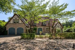 <p><em><strong>Karaktervol wonen in alle privacy, met Nederland binnen handbereik</strong></em></p>
<p>Een paar lengtes zwemmen voor het ontbijt. De tuindeuren openen op een zonnige ochtend. ’s Avonds vrienden ontvangen rond de tafel, terwijl het groen rondom stilaan in de schemer verdwijnt. In deze karaktervolle villa in de residentiële omgeving van Oud-Turnhout krijgt het dagelijkse leven alle ruimte. Op een perceel van ca. 2.724 m² woont u omringd door een aangelegde parktuin, met volledige privacy. Tegelijk geniet u hier van een uitstekende verbinding met Nederland. Een bijzonder aantrekkelijke uitvalsbasis voor wie over de grens werkt, onderneemt of regelmatig familie en vrienden bezoekt: thuiskomen in het groen, met uw leven aan weerszijden van de grens binnen handbereik.</p>
<p><strong>Een huis dat uitnodigt om te blijven</strong></p>
<p>De royale inkomhal met natuurstenen vloer zet meteen de toon. In de woonkamer zorgen hoge plafonds, authentieke moulures en rozetten voor karakter, terwijl het parket en de antieke schouw in Franse steen warmte toevoegen. Hier vindt u vanzelf uw favoriete plek: bij de haard met een boek, in de zithoek met het gezin of aan het raam met zicht op de tuin. Maatwerkkasten en een geïntegreerde muziekinstallatie vervolledigen het geheel.</p>
<p>Grote raampartijen trekken het groen naar binnen en verbinden de leefruimte met het terras. Dankzij de zuidoostelijke oriëntatie krijgt het daglicht hier een hoofdrol.</p>
<p>De aparte eetkamer sluit aan op de volledig uitgeruste leefkeuken. Onder het houten balkenplafond wordt de ontbijthoek al snel de plek waar iedereen samenkomt. Het Lacanche-gasfornuis, de kwalitatieve inbouwtoestellen en het natuurstenen werkblad nodigen uit om uitgebreid te koken. Van een snelle koffie voor vertrek tot een lang diner dat gerust wat later mag eindigen.</p>
<p><strong>Wellness op uw eigen ritme</strong></p>
<p>Voor ontspanning hoeft u de deur niet uit. Het binnenzwembad, stijlvol afgewerkt met natuursteen en voorzien van een aparte douchekamer en toilet, maakt zwemmen het hele jaar door mogelijk.</p>
<p>In de volledig ingerichte kelder gaat dat ontspannen verder. Een sauna, bar en smaakvolle wijnkelder bieden het decor voor een rustig wellnessmoment of een gezellige avond met vrienden. Deze verdieping is bereikbaar vanuit zowel de inkomhal als de zwembadruimte.</p>
<p><strong>Ruimte voor het gezin, gasten en eigen plannen</strong></p>
<p>Via de statige natuurstenen trap bereikt u de eerste verdieping. De ruime hoofdslaapkamer beschikt over parket, maatwerkkasten en een marmeren badkamer met dubbele wastafel, ligbad, inloopdouche, toilet en bidet.</p>
<p>Drie bijkomende slaapkamers en een tweede badkamer geven ieder gezinslid zijn eigen plek. De afzonderlijke was- en strijkkamer met ingemaakte kasten houdt het dagelijkse huishouden praktisch georganiseerd.</p>
<p>Op de bovenste verdieping bevindt zich een vijfde kamer, die u naar wens gebruikt als slaapkamer, bureau of hobbyruimte. Daarnaast is er een ruime bergzolder.</p>
<p><strong>Buiten leven, in alle beslotenheid</strong></p>
<p>De parktuin vormt een groen verlengstuk van de woning. Ontbijten op het terras, kinderen die in de tuin spelen of rustig genieten van de ruimte rondom: hier beleeft u elk seizoen op uw eigen manier. Achteraan biedt een ruim bijgebouw mogelijkheden als atelier, berging of multifunctionele ruimte.</p>
<p>Het volledig omheinde perceel is toegankelijk via een automatische poort. Vooraan is ruime parkeergelegenheid; de dubbele inpandige garage beschikt over automatische poorten. Vloerverwarming op het gelijkvloers, centrale verwarming op aardgas, camerabewaking en een alarmsysteem vervolledigen het comfort.</p>
<p><strong>Een villa voor wie royaal wil wonen, graag mensen ontvangt en thuis echt tot rust wil komen — met een uitstekende verbinding naar Nederland als dagelijkse troef.</strong></p>