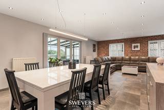 Voor meer info en foto’s, surf naar www.swevers.be – Deze ruime open bebouwing in Nieuwerkerken biedt met een bewoonbare oppervlakte van 239 m² alle comfort voor een groot gezin. De woning werd gebouwd in 1996 en ligt op een zuidgericht perceel van 8 are aan de Wouterveld 56. Via de inkomhal met gastentoilet bereikt u de lichtrijke leefruimte, waar zithoek, eetkamer en keuken mooi in elkaar overlopen. De keuken beschikt over voldoende werk- en bergruimte voor dagelijks gebruik. Op het gelijkvloers bevindt zich bovendien een ruime slaapkamer en een badkamer met ligbad en enkele wastafel. De eerste verdieping telt vier volwaardige slaapkamers van respectievelijk 18 m², 16 m², 16 m² en 16 m². Daarnaast is er een tweede badkamer met inloopdouche, toilet en een dubbele wastafel. De ruime open zolderverdieping op de tweede verdieping biedt tal van mogelijkheden als extra slaapkamer, hobbyruimte of extra opslagplaats. Ook praktisch scoort deze woning sterk dankzij de garage van 23 m² . Doorheen de jaren werd de woning zorgvuldig onderhouden en op verschillende vlakken vernieuwd. Daarnaast werden in 2018 zonnepanelen geplaatst, wat bijdraagt aan een lagere energiefactuur. Recente investeringen omvatten de plaatsing van een warmtepomp en een gaskachel in 2023, wat zorgt voor extra comfort en een efficiënte verwarming van de woning. Buiten geniet u van een zonnige, zuidgerichte tuin waar kinderen kunnen spelen en waar u optimaal kan genieten van lange zomeravonden. De ligging is bovendien bijzonder gunstig, met scholen en kinderopvang op wandelafstand, een bushalte op slechts 150 meter, winkels en ontspanningsmogelijkheden in de buurt en een vlotte verbinding naar het station en de autosnelweg. Bent u op zoek naar een ruime gezinswoning met vijf slaapkamers, twee badkamers, zonnepanelen en een zonnig perceel in Nieuwerkerken? Dan is deze woning zeker een bezoek waard. Voor meer informatie, bel 012 699 900. Bron bewoonbare oppervlakte: EPC – verslag