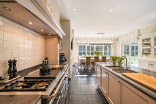 Op een van de meest gegeerde locaties van Schoten bevindt zich deze karaktervolle villa in Engelse landhuisstijl. Een oprijlaan in kasseien tussen hoogstammige bomen leidt naar de woning, die op een perceel van 2.183 m² omringd wordt door een prachtige tuin. Karakter en hedendaags comfort werden harmonieus gecombineerd op een bewoonbare oppervlakte van 615 m². Zo biedt de villa ruimte aan onder andere 5 slaapkamers, waarvan 3 met eigen dressing en ensuitebadkamer, een royale leefkeuken met ontbijthoek, een eetkamer, een bureau, een extra polyvalente ruimte, een recreatieruimte met biljart en bar, een wijnkelder en een dubbele garage.<br /><br />Gelijkvloers:<br />U betreedt de woning via een dubbele voordeur in natuurstenen omlijsting en de charmante inkomhal. Deze is afgewerkt met Belgisch blauwe hardsteen en geeft met zijn smeedijzeren trapleuning en open galerij een eerste blik op de verdieping. Van bij de eerste stap valt de authentieke Engelse sfeer op, versterkt door warm eiken parket in de leefruimtes en klassieke witte deuren met roedeverdeling.<br /><br />De hal geeft uit op de lichtrijke eetkamer, die via openslaande deuren rechtstreeks toegang geeft tot het terras en de tuin. Deze loopt verder door in de ruime living met een imposante natuurstenen schouw met open haard. Het geheel baadt in licht dankzij de hoge raampartijen.<br /><br />Het hart van de woning is de landelijke leefkeuken, met een groot kookeiland in Belgisch hardsteen en een Lacanche-fornuis, een blikvanger voor elke liefhebber van de kookkunst. De keuken loopt open over in de ontbijthoek, die dankzij de raampartijen langs drie zijden aanvoelt als een uitbouw in de tuin. Hier kunt u in elk seizoen genieten van het groen. Een praktisch bureau met ingebouwde kasten, een bergplaats en toegang tot de dubbele garage vervolledigen deze bouwlaag. Vanuit de keukenzone leidt een trap naar de wijnkelder.<br /><br />Eerste verdieping:<br />Via de trap met smeedijzeren balustrade bereikt men de ruime overloop met parket. De master bedroom beschikt over een ruime dressing en een ensuitebadkamer met bad, inloopdouche en dubbele lavabo, in klassieke stijl afgewerkt met lambrisering, metrotegels en hardsteen. Een tweede slaapkamer heeft een eigen badkamer. Een derde slaapkamer heeft een eigen dressing, een ensuitebadkamer en toegang tot een zonnig dakterras met zicht op het groen. Een praktische wasplaats met droogkast, een bergplaats en een apart toilet maken het geheel compleet.<br /><br />Ook op deze verdieping bevindt zich een bijzonder ruime kamer met hardstenen vloer, hoge plafonds en een sfeervolle kroonluchter. Dankzij het vele daglicht en de grote oppervlakte is ze veelzijdig inzetbaar, bijvoorbeeld als extra slaapkamer, speelkamer, studeerkamer of fitnessruimte.<br /><br />Tweede verdieping:<br />Op de tweede verdieping bevindt zich de recreatieruimte, met een ingebouwde bar in baksteen, een hardstenen vloer en veel daglicht via dakramen. Dit is de ideale plek voor een biljarttafel, een gezellige avond met vrienden of een speelruimte voor de kinderen. De technische ruimte en bijkomende zolderruimte vervolledigen deze bouwlaag.<br /><br />Buitenruimte:<br />De ruime tuin sluit rechtstreeks aan op de leefruimtes en vormt een oase van rust en privacy, dankzij het volwassen groen. Het royale terras aan de tuinzijde en het tuinhuis met overdekt terras nodigen uit tot een gezellig diner met vrienden of familie, terwijl de petanquebaan zorgt voor ontspanning. De dubbele garage met karaktervolle boogpoorten en de ruime oprijlaan bieden voldoende plaats voor het wagenpark.<br /><br />Technieken:<br />Ondanks de klassieke uitstraling is de villa volledig klaar voor de toekomst. Dankzij zonnepanelen, een warmtepomp, uitstekende isolatie en vloerverwarming behaalt de woning een EPC-label A. De elektrische keuring is in orde, waardoor de villa perfect instapklaar is.<br /><br />Bijzonderheden:<br />- Energiezuinig (EPC A) met zonnepanelen, warmtepomp en vloerverwarming<br />- Exclusieve villa op toplocatie<br />- 5 slaapkamers, waarvan 3 met dressing en ensuitebadkamer<br />- Leefkeuken met Lacanche-fornuis en kookeiland<br />- Extra polyvalente ruimtes, naar wens in te richten<br />- Belgisch blauwe hardsteen, eiken parket en natuurstenen schouw<br />- Zeer veel lichtinval en directe connectie met de tuin<br />- Elektrische keuring in orde, instapklaar<br /><br />Deze unieke woning in Schoten leert u het best kennen tijdens een persoonlijk bezoek. Contacteer Hillewaere en Christie's Real Estate voor een bezichtiging op afspraak en ontdek zelf het karakter, het licht en de rust van dit eigendom.