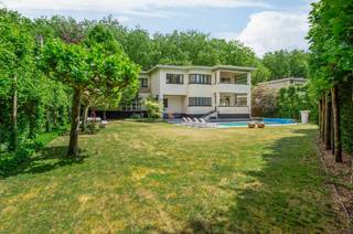 <p><span>Art-Deco villa met vele mogelijkheden op gunstige locatie</span></p><p><span>Deze verrassend ruime villa in typische Art-Deco stijl biedt vele mogelijkheden dankzij de grote leefruimtes en gunstige locatie. </span></p><p><span> </span></p><p><span>Indeling</span></p><p><span>U betreedt de villa middels de unieke ronde inkomhal met vide en daglicht via een dakraam. Vanuit deze centrale hal heeft u toegang tot de verschillende leefruimtes zoals de royale woonkamer met ensuite TV kamer, een apart bureel, een separate eetkamer met toegang tot het overdekt terras en vanuit de eetkamer ook een directe toegang tot de volledig uitgeruste keuken. </span></p><p><span> </span></p><p><span>1e Verdieping</span></p><p><span>De nachthal met gaanderij rondom de grote vide geeft toegang tot de verschillende kamers zoals een logeerkamer met toegang tot een dakterras, nog twee bijkomende ruime slaapkamers en een badkamer. Tevens een master suite bestaande uit een dressing, privatieve badkamer en slaapkamer met toegang tot een overdekt terras.</span></p><p><span> </span></p><p><span>Kelder</span></p><p><span>De woning is vrijwel volledig onderkelderd en biedt hiermee nog bijkomende mogelijkheden als bergruimte, alsook garage, hobbyruimte en technische ruimte.</span></p><p><span> </span></p><p><span>Tuin en buitenruimtes</span></p><p><span>Naast een dakterras en twee overdekte terrassen zijn er ook nog terrassen rondom het verwarmde zwembad. De tuin is omheind en geeft u voldoende rust en privacy. </span></p><p><span> </span></p><p><span>Bijzonderheden</span></p><p><span>Deze woning verkeert in een correcte staat van onderhoud en is voorzien van hedendaags comfort. Met enige inspanningen en/of investeringen kan deze villa een uniek eigendom zijn in haar soort.</span></p><p><span> </span></p><p><span>Meer inlichtingen via ons kantoor.</span></p>