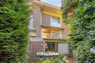 Ruime voormalige dokterswoning met praktijkruimte en tuinDeze voormalige dokterswoning biedt met maar liefst 352 m² bewoonbare oppervlakte, bijzonder veel ruimte en mogelijkheden. De combinatie van een voormalige praktijk op het gelijkvloers en ruime woonvertrekken op de verdiepingen maakt het pand uitermate geschikt voor wie wonen en werken onder één dak wil combineren. Indeling- Gelijkvloers: De woning beschikt over een inkomhal die toegang geeft tot de voormalige praktijkruimte, bestaande uit een wachtzaal, hal, afzonderlijk toilet en kabinet dat perfect dienst kan doen als bureau of professionele ruimte. Verder bevinden zich hier een voorraadberging, stooklokaal en een ruime garage met automatische poort.- Eerste verdieping: Via de hal met afzonderlijk toilet bereikt u de ruime en lichtrijke leefruimte (+/-54m²) met gezellige houthaard. Aan de straatzijde bevindt zich een klein terras. De keuken beschikt over een eigen eethoek en geeft toegang tot het ruime terras aan de tuinzijde. Een bijkomende kamer kan worden ingericht als bureau, speelkamer of hobbyruimte.- Tweede verdieping: de nachthal geeft toegang tot maar liefst vier slaapkamers (20,5m² - 17,6m² - 13m² - 10,5m²), een afzonderlijk toilet, linnenkamer, douchekamer en badkamer.- Exterieur: Achteraan beschikt de woning over een aangename tuin, bereikbaar via het terras aan de keuken. Karakteristieken- Voormalige dokterswoning met praktijkruimte- Vintage stijl- Zeer ruime woning van ca. 352 m²- Perceel van 2a 85ca- Afzonderlijke praktijk-/bureauruimtes- Ideaal om wonen en werken te combineren- Tal van berg- en functionele ruimtesEen woning met uitzonderlijk veel mogelijkheden. Ideaal voor een groot gezin, een vrij beroep of zelfstandige die wonen en werken wil combineren, maar evengoed voor wie simpelweg op zoek is naar een woning met veel ruimte. Mits de nodige opfrissing kan hier opnieuw een prachtige en veelzijdige gezinswoning worden gecreëerd. Contacteer ons via 02 460 80 46 of info@structura.be