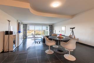 Uitzonderlijk doorloop-appartement in de prestigieuze residentie The Sanctuary, gelegen op de eerste lijn van het strand van Groenendijk te Oostduinkerke, op de grens met Nieuwpoort-Bad. Deze gegeerde ligging, pal aan zee en vlak bij surfclub Windekind, combineert rust, natuur en strandbeleving op een unieke manier.<br />De residentie werd in 1988 ontworpen door de gerenommeerde architect Marc Corbiau, wat zich vertaalt in een tijdloze architectuur met een sterke focus op licht, ruimte en zichtlijnen. Het appartement beschikt over een netto woonoppervlakte van 113 m² en maar liefst 35 m² aan terrassen. Vooraan bevindt zich een aangenaam terras met zicht op de duinen en de zee, terwijl aan de achterzijde een ruim en zonnig terras zorgt voor extra buitenruimte en privacy.<br />Het lichtrijke appartement is praktisch en comfortabel ingedeeld. Via de inkomhal met vestiaire en apart toilet betreedt u de leefruimte. De halfopen keuken is uitgerust met alle nodige apparatuur en sluit mooi aan op de ruime woonkamer, die dankzij grote raampartijen uitgeeft op het terras aan de voorzijde.<br />De nachthal biedt plaats aan een handige slaaphoek met ingemaakte kasten. Verder beschikt het appartement over een badkamer met dubbele wastafel, ligbad en toilet.<br />De eerste slaapkamer is voorzien van twee enkele bedden en een eigen badkamer met wastafel, douchecel en toilet. De tweede slaapkamer is voorzien van een tweepersoonsbed. Beide slaapkamers geven uit op het grote zuidgerichte terras aan de achterzijde.<br />Als extra troef is er een privatieve kelderberging inbegrepen en bestaat de mogelijkheid tot aankoop van een garagebox in de residentie. Daarnaast beschikt het gebouw over een gemeenschappelijke fietsenberging en een surfberging met douche, ideaal voor wie optimaal wil genieten van zee, strand en watersport.<br />Dankzij de unieke ligging aan het strand van Groenendijk, de royale oppervlaktes en de karaktervolle architectuur vormt dit appartement een bijzonder aantrekkelijke opportuniteit, zowel als tweede verblijf aan zee als voor wie op zoek is naar een ruim appartement op een absolute toplocatie. EPC: 450 kWh/m². Vraagprijs: 895000€