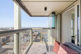 Op een unieke locatie aan het Kempisch Dok bevindt zich op de 22ste verdieping van de iconische Doktoren dit uitzonderlijke penthouse van ca. 132 m². Dankzij de ligging op de hoogste woonverdiepingen en de oriëntatie over drie zijden geniet u van indrukwekkende vergezichten, met als absolute blikvanger het frontale zicht over het Kempisch Dok en de Antwerpse skyline.
De inkomhal beschikt over een gastentoilet en geeft toegang tot de master bedroom met aangrenzend terras en elegante ensuite badkamer met lavabomeubel, inloopdouche en toilet. Daarnaast is er een praktische technische/wasruimte.
De lichtrijke leefruimte wordt gekenmerkt door kamerhoge beglazing en een open keuken die volledig geïnstalleerd is. Vanuit de leefruimte bereikt u het tweede terras, dat volledig met beglazing kan worden afgesloten en zo dienstdoet als aangenaam winterterras.
Aan de andere zijde bevinden zich twee bijkomende slaapkamers waarvan één momenteel als bureauruimte wordt gebruikt en ideaal is als home office. Een tweede badkamer met lavabomeubel en inloopdouche en een afzonderlijk toilet vervolledigen dit niveau.
Het appartement beschikt over vloerverwarming en privatieve zonnepanelen. Op de 23ste verdieping kunnen bewoners bovendien genieten van een gemeenschappelijk dakterras met een uniek panorama over Antwerpen en het omliggende waterlandschap.
Inclusief privatieve kelderberging. Een ondergrondse autostaanplaats dient verplicht bij aangekocht te worden voor € 40.000.