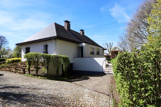 Deze karaktervolle woning is ruim ingedeeld en biedt bovendien de mogelijkheid om volledig gelijkvloers te kunnen wonen. <br />De verdieping beschikt over drie slaapkamers maar de grote zolderruimtes hebben nog veel uitbreidingsmogelijkheden. In de kelder is een grote garage en nog voldoende extra bergruimte. <br />De zichtlocatie is ideaal voor de ondernemer die op het gelijkvloers een kantoor/praktijk zou willen beginnen. De tuin naast de woning is gelegen in woongebied en zorgt nog voor extra potentieel. <br />De fijne, gezellige dorpskern met winkels, bakker en ontspanning ligt op wandelafstand. <br /><br />=> Gelijkvloers<br />- Royale inkomhal met dubbele deuren naar de leefruimte<br />- Deze hal is verrassend luchtig en heeft een apart gedeelte voor vestiaire met gastentoilet<br />- L-vormige woonkamer met prachtige parketvloer en open haard<br />- Het grote schuifraam aan de zijkant zorgt voor direct tuincontact en rechtstreekse toegang tot het groot overdekt terras<br />- Verzorgde en zeer degelijke keuken voorzien van alle gemak<br />- Rechtstreeks toegang naar de tuin en het terras vanuit de keuken <br />- Aansluitend is er een praktische en ruime bijkeuken met uitgietbak <br />- Grote slaapkamer aan de voorzijde van de woning toegankelijk vanuit de badkamer<br />- Betegelde badkamer met ligbad, dubbele wastafel in mooi badkamermeubel en apart af te sluiten toilet<br />- Naast de badkamer is er een aparte betegelde douchecel aanwezig <br /><br />=> Verdieping<br />- Ruime overloop met toegang tot de diverse slaapkamers en apart groot toilet met wastafel<br />- Er zijn drie mooie slaapkamers met vloerbekleding en allen voorzien van een eventuele aansluiting voor eigen wastafel op de kamer<br /><br />=> Zolder en kelder<br />- De grote zolderruimtes aan de zijkanten van de woning bieden nog voldoende uitbreidingsmogelijkheden indien gewenst<br />- De woning is deels onderkelderd met een toffe wijnkelder, bergruimtes en een grote garage <br /><br />=> Tuin<br />- De tuin bij deze woning situeert zich voornamelijk aan de zijkant van het huis en is fijn georiënteerd op het westen <br />- Dit perceel ligt volledig in woongebied hetgeen zorgt voor extra potentieel <br />- U kan via de oprit aan de zijkant van de woning de ondergrondse garage bereiken<br /><br />=> Indeling<br />- Gelijkvloers: inkomhal, aparte vestiaireruimte met gastentoilet, L-vormige woonkamer, keuken, bijkeuken/wasplaats, berging, aparte douchecel, badkamer met apart toilet, grote slaapkamer<br />- Verdieping: ruime overloop, drie slaapkamers, grote toiletruimte met wastafel, grote in te richten zolderruimtes<br />- Kelder: grote inpandige garage, wijnkelder, voorraadkelder, berging, kruipruimte