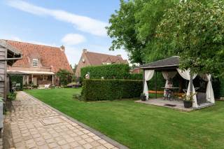 In een groene omgeving bevindt zich deze aangename vrijstaande woning met 4 ruime slaapkamers, een grote tuin en een dubbele garage. Een ideale gezinswoning voor wie op zoek is naar ruimte, comfort en mogelijkheden. <br /><br />Via de inkomhal komt u binnen in een ruime, open leefruimte met eet- en woonkamer. De gezellige recente gaskachel zorgt hier voor extra sfeer. Aansluitend bevindt zich de ruime en volledig uitgeruste keuken, voorzien van een vaatwasser, inductiekookplaat, microgolfoven, oven, koelkast en diepvriezer. Dankzij de vele kasten is er bovendien voldoende opbergruimte. Grenzend aan de keuken bevindt zich nog een gezellige ontbijthoek.<br /><br />Op het gelijkvloers bevinden zich verder een ruime bureau/praktijkruimte (26m²), wasplaats, gastentoilet en vestiaire.<br /><br />Op de eerste verdieping bevinden zich vier ruime slaapkamers (14 m², 14 m², 18 m² en 19 m²). De badkamer beschikt over een bad, inloopdouche en dubbele lavabo. Bovendien is er nog een grote zolder die extra bergruimte biedt.<br /><br />Via een poort op de oprit bereikt u de dubbele garage. Aansluitend bevindt zich de prachtige ruime tuin met een overdekt terras, twee paviljoentjes en een tuinhuis met werkplaats.<br /><br />Pluspunten:<br />+ Groene omgeving<br />+ 4 ruime slaapkamers<br />+ Dubbele garage<br />+ Prachtige tuin<br />+ Grote zolder<br /><br />Heeft u interesse en wenst u een bezoek ter plaatse in te plannen? Aarzel niet ons te contacteren op het nummer 03 337 50 70 of via info@vbvastgoed.be.