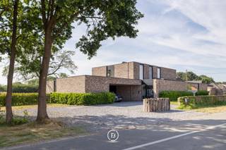 Deze stijlvolle, moderne villa uit 2018 is gelegen op een uitzonderlijk breed perceel van maar liefst 5.016 m² en biedt een unieke combinatie van hedendaags wooncomfort, privacy en een groene, landelijke omgeving. De tijdloze architectuur, gekenmerkt door grote raampartijen, zorgt voor een overvloed aan natuurlijk licht en creëert een harmonieuze verbinding tussen binnen en buiten.<br /><br />Het royale perceel vormt een absolute meerwaarde voor wie houdt van ruimte en natuur. Dankzij de omvang en de rustige ligging biedt het tal van mogelijkheden voor dierenliefhebbers en paardenliefhebbers, met voldoende plaats om dieren aan huis te houden of het terrein naar eigen wens in te richten.<br /><br />Ook voor wie wonen en werken wil combineren, is deze woning bijzonder geschikt. Er zijn twee afzonderlijke ruimtes voorzien die perfect kunnen dienen als praktijk, bureau of kantoor aan huis.<br /><br />De leefruimte werd ontworpen met oog voor openheid, licht en wooncomfort. De volledig uitgeruste keuken is voorzien van hoogwaardige Gaggenau-toestellen en een Quooker-kraan. Vanuit de keuken en de aangrenzende leefruimte geniet u van een prachtig, weids uitzicht over de zuidoost georiënteerde tuin en de achterliggende natuur, waardoor elk seizoen optimaal beleefd kan worden.<br /><br />Aansluitend aan de keuken bevindt zich een ruime berging die eveneens rechtstreeks bereikbaar is via de carport. Daarnaast beschikt de woning over talrijke maatkasten, een tweede grote berging en een aparte wasruimte met douche, waardoor functionaliteit en opbergruimte ruimschoots aanwezig zijn.<br /><br />Het wooncomfort wordt verder versterkt door een uitgebreid domoticasysteem, camerabewaking, een alarmsysteem en een geïntegreerde muziekinstallatie die doorheen de volledige woning voor extra gebruiksgemak en sfeer zorgen.<br /><br />De villa telt vijf volwaardige slaapkamers en twee stijlvolle badkamers. De master bedroom beschikt over een ensuite badkamer en een ruime dressing, met een rustgevend uitzicht op het omliggende groen.<br /><br />Ook op technisch vlak voldoet deze woning aan de hoogste verwachtingen. Dankzij het gunstige energielabel A en de conforme elektrische installatie is deze villa volledig klaar voor de toekomst.<br /><br />Deze uitzonderlijke eigendom biedt een zeldzame combinatie van moderne architectuur, hoogwaardig wooncomfort, een prachtig natuurzicht en een royaal perceel met tal van mogelijkheden voor gezinnen, zelfstandigen én dieren- of paardenliefhebbers.