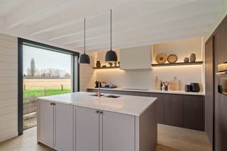 Deze hoogwaardig afgewerkte nieuwbouwwoning, te koop onder het gunstige stelsel van registratierechten, ligt op een uitstekend bereikbare en toch zeer groene locatie in Hansbeke. Het zorgvuldig aangelegde perceel vormt een natuurlijk verlengstuk van de woning en biedt een prachtig, rustgevend panorama over de omliggende natuur.<br /><br />Bij binnenkomst verwelkomt de ruime inkomhal met gastentoilet u en zet meteen de toon voor de rest van het huis. De open leefkeuken met kwaliteitsvolle toestellen vormt het hart van de woning en sluit naadloos aan op de eetplaats en leefruimtes. Dankzij de grote raampartijen, volledig georiënteerd op de tuin, vloeien binnen- en buitenleven harmonieus in elkaar over. De leefruimtes zijn voorzien van vloerverwarming voor optimaal comfort. Aansluitend bevindt zich een praktische wasplaats met extra bergruimte en buitendeur.<br /><br />Op de eerste verdieping vindt u drie volwaardige slaapkamers en twee badkamers. De master bedroom biedt luxe met een eigen dressing en ensuite badkamer. De twee overige slaapkamers delen een tweede, ruime badkamer met ligbad.<br /><br />De hoger gelegen verdieping herbergt een riante, multifunctionele ruimte die kan dienen als extra slaapkamer, kantoor of hobbyruimte.<br /><br />Naast de woning staat een kwalitatief afgewerkte garage, momenteel ingericht als inspirerend thuiskantoor. Deze eigendom staat garant voor een doordachte indeling en uitzonderlijke afwerking.<br /><br />Meer info en 3D-tour op www.hillewaere-vastgoed.be