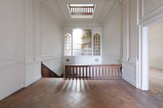 <p>Aan de Frankrijklei staat dit statige herenhuis met een verfijnde lijstgevel, sierlijke smeedijzeren balkons en een leien mansardedak met ronde dakvensters.</p>
<p>Een adembenemende inkomhal met dubbele plafondhoogte. Een brede eikenhouten trap met sierlijk gedraaide balusters en een fraai gebeeldhouwde trappaal leidt, langs een lambrisering in massief hout, naar de bovenverdiepingen. De vloer is afgewerkt met visgraatparket. Hoog boven de trap vangt een monumentaal glas-in-loodraam het licht: een negentiende-eeuws pronkstuk. Rijk gestucte plafonds en kroonlijsten versterken het karakter van het eigendom.</p>
<p>Vanuit de hal geeft een dubbel openslaande deur toegang tot een lichtrijk salon, waar een verfijnde marmeren haardmantel met een sierlijke overschouw de blikvanger vormt. Het visgraatparket, de hoge plafonds en de verzorgde lambrisering zetten de sfeer van de inkomhal verder door op de gelijkvloerse verdieping.<br />Het pand telt 6 ruime slaapkamers en 3 badkamers, verspreid over de bovenverdiepingen. De overloop op de eerste verdieping vormt een verlengstuk van de inkomhal: een statige ruimte met witte lambriseringen en hetzelfde prachtige glas-in-loodraam. Boven de traphal zorgt een glazen lichtstraat, met zicht op de balustrade van de bovenverdieping, voor een verrassende lichtinval tot diep in het huis.</p>
<p>Achteraan opent het huis zich op een verrassend groene stadstuin – een zeldzaamheid voor een pand aan de Leien. Een gietijzeren balustrade in Belle Époque-stijl siert het terras aan de achtergevel waarbij een buitentrap naar de tuin afdaalt. <br />Achteraan de tuin ligt het koetshuis: een sfeervol tuinpaviljoen. Vandaag leent dit karaktervolle bijgebouw zich uitstekend als atelier, kantoor aan huis of gastenverblijf.</p>
<p>Het pand is volledig onderkelderd, wat bijkomende bergruimte en technische mogelijkheden biedt.</p>
<p>De Frankrijklei maakt deel uit van de Leien, de negentiende-eeuwse boulevards rond de historische Antwerpse binnenstad. Zeer centraal gelegen nabij Botanische tuin, Theaterplein en het Zuid.</p>
