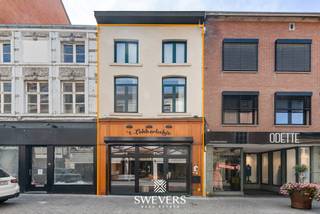 Voor meer info en foto’s, surf naar www.swevers.be – Op een centrale locatie aan de Stapelstraat 38 in Sint-Truiden bevindt zich dit instapklare handelshuis, ideaal voor ondernemers die op zoek zijn naar een commerciële uitvalsbasis met veel opslag- en werkruimte. Het pand beschikt over een bruikbare oppervlakte van 272 m² op een perceel van 1a 06ca en combineert de charme van een historisch gebouw met hedendaags comfort dankzij verschillende renovaties. Op het gelijkvloers bevindt zich de winkelruimte met achteraan een ruime keuken van 41,47 m², twee afzonderlijke koelcellen en een apart toilet. De eerste verdieping biedt een bureau, technische ruimte, berging en ongeveer 78 m² opslagruimte. Op de tweede verdieping is er nog een extra opslagplaats van circa 33 m², terwijl de ingerichte zolder van 26 m² bijkomende mogelijkheden biedt voor stockage of ondersteunende activiteiten. Het pand werd doorheen de jaren grondig vernieuwd. In 2000 werden onder meer de elektriciteit, gasinstallatie en winkelinrichting vernieuwd. In 2018 volgden een nieuw dak en de afwerking van de tweede verdieping en zolder. In 2023 werden 9 zonnepanelen geplaatst en het volledige gebouw uitgerust met energiezuinige ledverlichting. Er is een mogelijkheid tot overname van het handelsfonds voor 45.000 euro. De ligging is een grote troef: op slechts 500 meter van de Grote Markt, met winkels en restaurants op wandelafstand en een vlotte bereikbaarheid via openbaar vervoer en de snelwegen. Een uitstekende opportuniteit voor wie een instapklare commerciële eigendom zoekt op een toplocatie in Sint-Truiden. Voor meer informatie, bel 012 699 900. Bron bewoonbare oppervlakte: EPC – verslag.