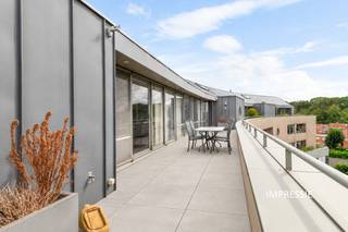 In het centrum van Brasschaat bevindt zich dit bijzonder ruime en lichtrijke penthouse, ontworpen door architect Jef Van Oevelen. Het appartement combineert een hoogwaardige afwerking met royale leefruimtes, twee terrassen en een uitzonderlijk centrale ligging. Winkels, supermarkten, restaurants, de bibliotheek en het Park van Brasschaat bevinden zich allemaal op wandelafstand.<br /><br />Via de lift bereiken we rechtstreeks de ruime inkomhal van het appartement, afgewerkt met een tegelvloer. Van hieruit betreden we de indrukwekkende leefruimte van ca. 95 m², voorzien van massief eiken parket. De grote raampartijen over de volledige breedte zorgen voor een bijzonder aangename lichtinval en geven rechtstreeks toegang tot het ruime zuidwestgerichte dakterras van ca. 38 m², met panoramisch zicht over Brasschaat.<br /><br />Aansluitend aan de leefruimte bevindt zich een tweede salon/tv-ruimte van ca. 31 m², voorzien van een ingemaakte tv- en barkast en aansluiting voor speakers. <br /><br />De volledig geïnstalleerde keuken beschikt over een kookeiland met eethoek en is uitgerust met onder meer een inductiekookplaat, vaatwasser, oven, stoomoven en ingebouwde friteuse van Miele. Dankzij de vele ingemaakte kasten is er bovendien voldoende bergruimte voorzien. Vanuit de keuken is er toegang tot een tweede terras van ca. 6 m².<br />Aansluitend bevindt zich een praktische bijkeuken/wasplaats met aansluitingen voor wasmachine en droogkast.<br /><br />Verder beschikt het appartement over een gastentoilet met lavabo en een afzonderlijke bureauruimte van ca. 20 m², volledig op maat uitgevoerd in notenhout.<br />Deze ruimte kan indien gewenst worden ingericht als volwaardige slaapkamer.<br /><br />Het nachtgedeelte omvat een royale dressing die toegang geeft tot de master bedroom. Aansluitend bevindt zich de ensuite badkamer, uitgerust met een notenhouten lavabomeubel met twee opzetwastafels, een ruime inloopdouche en toilet.<br /><br />Via een vaste trap is bovendien nog een zolderverdieping bereikbaar, die bijkomende bergruimte biedt.<br /><br />Het appartement werd doorheen de jaren bijzonder goed onderhouden en is afgewerkt met kwalitatieve materialen en tal van ingemaakte kasten. Het beschikt over vloerverwarming met afzonderlijke circuits, gasverwarming via een Viessmann-installatie en airconditioning doorheen het appartement. <br /><br />Bij het appartement zijn tevens een dubbele garagebox met automatische poort en een private kelderberging inbegrepen.<br /><br />Troeven:<br />+ Centrale ligging in Brasschaat<br />+ Royale en lichtrijke leefruimte van ca. 95 m²<br />+ Zuidwestgericht dakterras van ca. 45 m²<br />+ Tweede terras van ca. 6 m²<br />+ Vloerverwarming en airconditioning<br />+ Dubbele garagebox met automatische poort<br />+ Private kelderberging<br />+ Gunstig EPC – B<br /><br />Interesse in dit appartement?<br />Contacteer ons via 03 337 50 70 of info@vbvastgoed.be voor meer info of een bezoek ter plaatse.