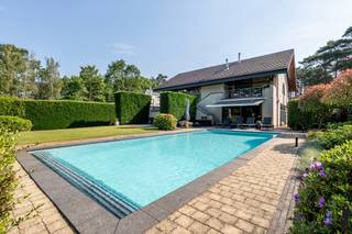 <p><strong>Exclusieve split-levelvilla met 5 slaapkamers, zwembad en prachtig aangelegde tuin</strong></p>
<p>Wie op zoek is naar een woning met <strong>karakter</strong>, <strong>uitzonderlijke volumes</strong> en een <strong>unieke woonbeleving</strong>, zal onmiddellijk gecharmeerd zijn door deze <strong>indrukwekkende split-levelvilla</strong>. Dankzij haar <strong>speelse architectuur</strong>, <strong>royale leefruimtes</strong> en <strong>prachtige buitenomgeving</strong> biedt deze eigendom een <strong>zeldzame combinatie van luxe, comfort en functionaliteit</strong>.</p>
<p>Vanaf het eerste moment valt de <strong>bijzondere indeling</strong> van de woning op. De verschillende niveaus creëren een natuurlijke scheiding tussen wonen, slapen, werken en ontspannen, terwijl de open verbindingen zorgen voor een aangenaam gevoel van <strong>ruimte en licht</strong>. <strong>Grote raampartijen</strong> laten het daglicht overvloedig binnenstromen en bieden op verschillende plaatsen een prachtig zicht op de tuin en de omliggende <strong>groene omgeving</strong>.</p>
<p>Het absolute middelpunt van de woning is zonder twijfel de <strong>uitzonderlijk ruime woonkamer</strong> van maar liefst circa <strong>83 m²</strong>. Dankzij de directe toegang tot het <strong>ruime terras</strong> vloeien <strong>binnen- en buitenleven</strong> naadloos in elkaar over.</p>
<p>Een niveau hoger bevindt zich de <strong>ruime leefkeuken</strong> die perfect aansluit op de aangename eetruimte. Deze combinatie vormt het <strong>kloppende hart van het huis</strong> waar koken, tafelen en samenzijn centraal staan.</p>
<p>De villa telt maar liefst <strong>vijf volwaardige slaapkamers</strong>, verspreid over verschillende niveaus. Hierdoor geniet ieder gezinslid van voldoende <strong>privacy en comfort</strong>. De <strong>hoofdslaapkamer van circa 33 m²</strong> vormt een echte <strong>privésuite</strong> met een royaal gevoel van ruimte en rust.</p>
<p>Verder beschikt de woning over een <strong>ruime badkamer</strong> met ligbad en douche, meerdere sanitaire voorzieningen en een afzonderlijke wasruimte, wat het dagelijkse comfort aanzienlijk verhoogt.</p>
<p>Voor wie van thuis uit werkt of extra ruimte nodig heeft voor een praktijk, hobby of creatieve activiteiten, biedt de woning een <strong>uitzonderlijk ruime kantoorruimte</strong> van ongeveer <strong>31 m²</strong>.</p>
<p>Buiten ontvouwt zich een ware <strong>oase van rust en privacy</strong>. De <strong>grote, perfect onderhouden tuin</strong> vormt een groene omgeving waar jong en oud het hele jaar door kunnen genieten. Centraal in de tuin ligt het <strong>zwembad</strong>, dat tijdens de zomermaanden garant staat voor <strong>ontspanning</strong> en een echt <strong>vakantiegevoel in eigen huis</strong>. De verschillende terrassen rond de woning bieden op elk moment van de dag een aangename plek om te genieten van de zon of de schaduw.</p>
<p>De architectuur van deze split-levelvilla zorgt niet alleen voor een bijzonder ruimtelijk gevoel, maar geeft de woning ook een <strong>unieke uitstraling</strong> die haar onderscheidt van klassieke villa's.</p>
<p><strong>Troeven op een rij</strong></p>
<p>✔ Exclusieve split-levelarchitectuur<br />✔ 5 ruime slaapkamers<br />✔ Ruime kantoorruimte<br />✔ Verschillende terrassen<br />✔ Grote zolder met uitbreidingsmogelijkheden<br />✔ Perfect onderhouden en aangelegde tuin<br />✔ Verwarmd zwembad<br />✔ Veel natuurlijke lichtinval</p>
<p><strong>Een bezoek zal u zonder twijfel overtuigen van de uitzonderlijke kwaliteiten van deze eigendom.</strong></p>