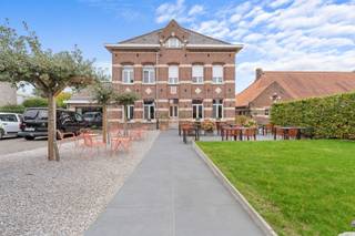 In het centrum van Nieuwkerke bevindt zich deze bijzondere voormalige directeurswoning uit 1923. Een karaktervolle eigendom waarin authentieke elementen, royale ruimtes en hedendaags comfort op een mooie manier samenkomen. De statige gevel, hoge plafonds en bewaarde originele details geven het pand een unieke uitstraling. Dankzij de centrale ligging en de veelzijdige indeling leent deze eigendom zich uitstekend voor verschillende doeleinden. Naast een ruime gezinswoning behoort ook een combinatie van wonen en werken, een B&amp;B-concept of een horecazaak met woongelegenheden tot de mogelijkheden.<br /><br />Bij binnenkomst zorgt de inkomhal meteen voor een aangename eerste indruk. Op het gelijkvloers bevindt zich momenteel een sfeervol restaurantgedeelte met plaats voor 34 gasten. Aan de voorzijde sluit het zonnige terras hier mooi op aan, met ruimte voor ongeveer 40 personen. De volledig uitgeruste bar en professionele keuken vormen samen een praktische en sfeervolle horecaruimte. Vanuit de bar is er bovendien toegang tot een ruime kelder, ideaal als extra opslagruimte.<br /><br />De eerste verdieping omvat een comfortabel appartement met een bijzonder lichtrijke leefruimte en mooi uitzicht over de tuin en de omgeving van Nieuwkerke. Daarnaast beschikt deze verdieping over een bureauruimte, een ruime slaapkamer met rechtstreekse toegang tot de badkamer en een afzonderlijke, volledig ingerichte keuken. De badkamer is uitgerust met een dubbele lavabo, inloopdouche en toilet.<br /><br />Ook de tweede verdieping werd ingericht als volwaardig appartement. Hier zorgen de open indeling en de vele lichtinval voor een aangename woonbeleving. De leefruimte sluit rechtstreeks aan op de keuken en de ruime slaapkamer beschikt over een open badkamer, wat zorgt voor een eigentijdse loftsfeer. Een bijkomende badkamer met dubbele lavabo, toilet en inloopdouche biedt het nodige comfort.<br /><br />Achteraan bevindt zich een verrassend ruime en groene tuin, een rustige plek midden in het centrum. Het voorste gedeelte doet momenteel dienst als terras voor het restaurant. Verder zijn er twee ruime bergingen aanwezig, waarvan één voorzien is van een pizzaoven. Deze ruimtes bieden tal van mogelijkheden voor opslag, hobby's of een creatieve invulling. Daarnaast beschikt de tuin over een verzorgde moestuin en kippenren. Een bijkomende troef is de achteruitgang naar de Steenwerkstraat, samen met parkeermogelijkheid naast het pand. Zo combineert de eigendom een centrale ligging met een uitzonderlijk ruime buitenomgeving.<br /><br />In 2017 werd het pand grondig gerenoveerd, waarbij veel aandacht werd besteed aan het behoud van het authentieke karakter én het hedendaagse comfort. Zo werden onder meer de leidingen vernieuwd, het dak aangepakt en een ventilatiesysteem en zonnepanelen geplaatst. Ook werden waterverzachter en brandwerende plafonds en deuren voorzien.<br /><br />Een eigendom met geschiedenis, uitstraling en bijzonder veel mogelijkheden. Of u nu op zoek bent naar een ruime woning, een karaktervol horecapand, een B&amp;B-concept of een combinatie van wonen en werken: deze voormalige directeurswoning biedt een unieke basis in het hart van Nieuwkerke. Interesse in dit veelzijdige pand? Contacteer ons vandaag nog voor meer informatie of een bezoek ter plaatse.