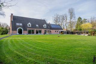 <p><strong>Riante gerenoveerde pastorijwoning met garage, studio en wellness op een perceel van ca. 5.400 m²</strong></p>
<p>Deze prachtige pastorijwoning werd volledig gerenoveerd en is gelegen op een ruim en privatief perceel van ca. 5.400 m². De woning combineert karakter met hedendaags comfort en beschikt over 4 à 5 slaapkamers, 3 badkamers, een ruime garage met studio en een aangelegde tuin met wellness.</p>
<p>De woning omvat:</p>
<ol>
<li>Een gelijkvloerse verdieping met o.a. inkomhal, leefruimte, open keuken, bureel/slaapkamer en badkamer.</li>
<li>Een eerste verdieping met meerdere slaapkamers en badkamers.</li>
<li>Een garagegebouw met studioverdieping.</li>
</ol>
<p><strong>Voorzieningen op het gelijkvloers:</strong><br />Deze woning is op het gelijkvloers voorzien van:<br />- Een ruime inkomhal op parket met vestiairekast en gastentoilet met handenwasser<br />- Een eerste slaapkamer met ensuite badkamer voorzien van inloopdouche, toilet en lavabo<br />- Een tweede kamer, ideaal als bureel of extra slaapkamer.<br />- Een lichtrijke leefruimte met open haard en grote schuiframen met toegang tot de tuin.<br />- Een open, volledig ingerichte keuken met o.a. dubbele spoelbak, vaatwasser, gasfornuis met oven, dampkap, Amerikaanse koelkast en wijnkoelkast.</p>
<p><strong>Voorzieningen op de eerste verdieping:</strong><br />De eerste verdieping bestaat uit:<br />- Twee ruime slaapkamers.<br />- Een badkamer met douche, toilet en lavabo, alsook aansluitingen voor wasmachine en droogkast.<br />- Een master bedroom met dressing en ensuite badkamer voorzien van ligbad, inloopdouche, dubbele lavabo en toilet.<br />- Twee praktische bergruimtes op de overloop.</p>
<p><strong>Garage en studio:<br /></strong>- Ruime inpandige garage met automatische poorten en plaats voor drie wagens.<br />- Boven de garage bevindt zich een studioverdieping, bereikbaar via een vaste trap.</p>
<p><strong>Tuin:</strong><br />Aangelegde en privatieve tuin bereikbaar via een automatische toegangspoort en lange oprit met parkeermogelijkheden voor meerdere wagens. De tuin beschikt over een siervijver met terras, een open achterliggend perceel met mooie bomen, een overdekt terras, een aanbouw met glaspartijen en een buitenwellness met sauna, douche en koelbad.<br />Tussen de woning en de garage bevindt zich een overdekte carport.</p>
<p><strong>Extra troeven:<br /></strong>- Zeer ruim perceel met veel privacy<br />- Groot bewoonbaar volume<br />- Drievoudige garage<br />- Veel lichtinval<br />- Kruipruimte onder de volledige woning<br />- Gunstig EPC</p>