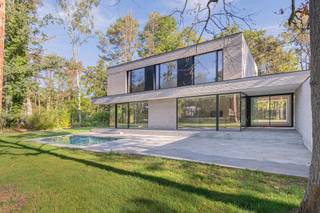 Diep verscholen in het groen, aan het einde van een discrete oprit, bevindt zich deze uitzonderlijke nieuwbouwvilla op een riant perceel van ca. 3.000 m². Dit architecturaal meesterwerk onderscheidt zich door zijn pure vormgeving, zeldzame rust en hoogwaardige materiaalkeuze — een toonbeeld van hedendaagse luxe, zonder in te boeten op warmte of leefbaarheid.<br /><br />De villa werd opgetrokken in een horizontaal metselverband met lichte, genuanceerde gevelsteen. De strakke volumewerking wordt verzacht door de overvloedige glaspartijen die van vloer tot plafond reiken. Ze zorgen niet alleen voor een adembenemende lichtinval, maar creëren ook een naadloze connectie tussen binnen en buiten. De tuin met vijver én zwembad zorgen voor verkoeling op warme dagen.<br /><br />Via de inkomhal betreed je de royale leefruimte met aangename plafondhoogte. De open leefkeuken — op maat ontworpen en voorzien van alle denkbare high-end toestellen — sluit naadloos aan op de living. Grote schuiframen openen naar het zonneterras en het strak geïntegreerde zwembad, ideaal georiënteerd op het zuiden.<br /><br />Op het gelijkvloers vinden we verder nog een gastentoilet, berging, technische ruimte en inpandige fietsenstalling — subtiel ingewerkt in de structuur van het gebouw.<br /><br />De verdieping omvat:<br /><br />- een royale slaapkamer met dressing en ensuite badkamer (inloopdouche, dubbele wastafel, vrijstaand bad)<br /><br />- twee ruime kinderkamers met ingebouwde kasten<br /><br />- een tweede badkamer en apart toilet<br /><br />Elke ruimte ademt rust, licht en verfijning.<br /><br />De villa is bovendien discreet gelegen in een doodlopende straat. Hier geniet u absolute rust en privacy in een groene oase, op wandelafstand van de prestigieuze Golf Club Keerbergen. De combinatie van deze topligging en het unieke architecturale concept maken deze eigendom ronduit zeldzaam.<br /><br />Een huis dat niet enkel ontworpen is om in te wonen, maar om in te leven.