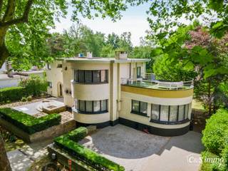 Karaktervolle Art-Deco villa met potentieel op toplocatie<br />In een geliefde en goed bereikbare omgeving vindt u deze ruime villa in authentieke Art-Deco stijl (vroeger dokterswoning) Dankzij de royale ruimtes en veelzijdige indeling biedt deze woning tal van mogelijkheden voor wie op zoek is naar comfort én karakter.<br />De entree maakt meteen indruk: een ronde inkomhal met vide, waar het daglicht via een dakraam prachtig naar binnen valt. Vanuit deze hal bereikt u een riante woonkamer die naadloos aansluit op een gezellige tv-kamer. Verder zijn er een afzonderlijk bureel, een aparte eetkamer met toegang tot het overdekte terras én een volledig ingerichte keuken die eveneens rechtstreeks vanuit de eetkamer toegankelijk is.<br />Op de bovenverdieping verbindt een gaanderij, die rond de vide loopt, alle kamers met elkaar. Er is een logeerkamer met dakterras, twee ruime slaapkamers en een badkamer. De master suite beschikt over een dressing, een privébadkamer en een slaapkamer met toegang tot een tweede overdekt terras.<br />De villa is nagenoeg volledig onderkelderd, wat extra ruimte oplevert voor opslag, een garage, hobbyruimte en technische voorzieningen.<br />Naast het dakterras en de twee overdekte terrassen vindt u meerdere zonneterrassen rond het verwarmde zwembad. De omheinde tuin garandeert volledige privacy en een rustige setting.<br />De woning is goed onderhouden en uitgerust met hedendaags comfort. Met enkele gerichte verbeteringen kan dit pand uitgroeien tot een werkelijk uniek eigendom binnen zijn klasse.<br />EPC C, G en P score : A,