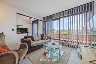 Voor meer info en foto’s, surf naar www.swevers.be – Op Markt 17 bus 7 in Heppen bevindt zich dit ruime appartement met een bewoonbare oppervlakte van 55 m². Het appartement dateert van 1996, verkeert in opgefriste staat en combineert een praktische indeling met twee aangename terrassen. De leefruimte van maar liefst 42,46 m² vormt het centrale gedeelte van het appartement en biedt voldoende plaats voor een volwaardige zit- en eethoek. Aansluitend bevindt zich de gedeeltelijk open keuken van 6,21 m². Grote raampartijen zorgen voor veel contact met het langgerekte terras, dat zich over nagenoeg de volledige breedte van het appartement uitstrekt. Verder beschikt het appartement over één slaapkamer van 9,67 m², met toegang tot een tweede en ruimer terras. Naast de slaapkamer ligt de badkamer met douche en wastafel. Het toilet bevindt zich praktisch in een afzonderlijke ruimte. Extra comfort wordt geboden door airconditioning, jaloezieën, lift in het gebouw en aparte garagebox. Ook de ligging is praktisch: restaurants bevinden zich vanaf circa 100 meter, openbaar vervoer op 300 meter, scholen op 450 meter en winkels op ongeveer 650 meter. De snelwegen liggen op circa 8 kilometer. Een ruim appartement met een grote living, twee terrassen en een centrale ligging in Heppen. Ideaal voor wie comfortabel wil wonen met alle nodige voorzieningen binnen handbereik. Voor meer informatie, bel 011 255 155. Bron bewoonbare oppervlakte: EPC – verslag.