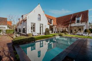 Beleef de perfecte symbiose tussen traditie en luxe in deze villa (2017), ontworpen door architect Stéphane Boens. Gelegen op een zonovergoten perceel van ca. 1.000 m² in een rustige residentiële wijk, bevindt u zich op wandelafstand van de zee en het centrum van Koksijde. De woning combineert klassiek vakmanschap, zoals metselwerk in wildverband, afgeronde muren, unieke raamopeningen die het daglicht prachtig naar binnen gidsen en smeedijzeren details, met hedendaagse luxe. Een uniek eigendom waar authentiek vakmanschap en modern wooncomfort op hoog niveau samenkomen.Het private gedeelte omvat een leefruimte met open haard, een luxueuze leefkeuken met gashaard voorzien van panoramisch zicht op de tuin en een master-suite die beschikt over een eigen luxebadkamer met bad, douche en dubbele lavabo op het gelijkvloers. Op de verdieping bevinden zich nog twee slaapkamers met badkamer en een polyvalente ruimte die naar wens kan dienen.Het B&B-gedeelte beschikt over een eigen inkom, een sfeervolle eetruimte en drie gastenkamers met elk een ensuite badkamer. Dankzij de praktische indeling kan dit gedeelte bovendien perfect worden ingericht als volwaardig privatief woongedeelte. De zuidwestelijk georiënteerde tuin is een oase van rust, waar u het hele jaar door geniet van maximale zoninval. Het middelpunt is het schitterende zwembad (7 x 3,5 m). Voor de ultieme ontspanning kunt u afdalen naar de kelderverdieping, die is ingericht als een volwaardige wellness met een sauna, hamam, douche en toilet.Benieuwd naar deze villa? Plan dan in uw afspraak in bij Carl Boedts (0473/951821) of Yari Devos (0491/272185).