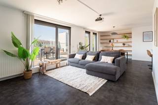 Deze instapklare penthouse is gelegen in de Lange Sint-Annastraat, een karaktervolle straat in het hart van Antwerpen, op het kruispunt van het Eilandje, de universiteitswijk en het historische centrum. Stijlvolle winkels, kwalitatieve horeca en culturele hotspots bevinden zich op wandelafstand, net als de Meir, Groenplaats en Grote Markt. Dankzij deze centrale ligging geniet u van het bruisende stadsleven, terwijl u bovenaan het gebouw in alle rust thuiskomt. Zowel openbaar vervoer als belangrijke invalswegen zijn vlot bereikbaar.<br /><br />Het appartement bevindt zich op de bovenste verdieping van een recente en verzorgde residentie. De lichtrijke leefruimte vormt het hart van het appartement en geeft via grote raampartijen toegang tot twee ruime zonneterrassen aan weerszijden. Dit zorgt de hele dag door voor overvloedig natuurlijk licht en een aangenaam panoramisch uitzicht over de stad. Aansluitend aan de leefruimte bevindt zich een aparte bureauruimte, ideaal als thuiswerkplek of in te richten als derde slaapkamer.<br /><br />De keuken is volledig uitgerust met kwalitatieve toestellen en een ruim werkblad, perfect voor wie graag kookt en gasten ontvangt. Verder beschikt het appartement over twee ruime slaapkamers, een modern afgewerkte badkamer met ligbad, inloopdouche en dubbel lavabomeubel, een apart gastentoilet en een praktische (was) berging. <br />Een privatieve kelderberging en gemeenschappelijke fietsenberging zijn inbegrepen. De aankoop van een ondergrondse autostaanplaats is mogelijk.