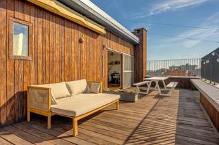 <strong>Algemeen</strong><br />Op de zesde en zevende verdieping, helemaal bovenaan het gebouw, ligt dit duplex-penthouse van ca. 211 m². Het voelt eerder als een huis in de lucht dan als een appartement. Beneden is het rustig, met drie slaapkamers, een aparte dressing, een badkamer en veel ingemaakte kasten. Boven ligt één grote, lichte leefruimte met witgeschilderde balken, een industriële keuken, een vierde slaapkamer, een tweede badkamer en twee terrassen van samen zo’n 70 m². Een smeedijzeren wenteltrap verbindt de twee verdiepingen. Ook technisch zit het goed: het dak van het gebouw werd gerenoveerd, de verwarmingsketel is pas vernieuwd en het appartement heeft een EPC-label C. Er is een lift, en bij het appartement horen twee kelders.<br /><strong>Ligging</strong><br />Het penthouse ligt aan het begin van de Turnhoutsebaan, op het kruispunt met de Carnotstraat en de Kerkstraat. Het Centraal Station, het Astridplein en de Zoo liggen op een paar minuten wandelen. Winkels, bakkers, koffiebars en restaurants vind je in alle richtingen, en tram en bus stoppen vlakbij. Je woont hier in het hart van de stad, maar vanaf de bovenste verdieping hoor je de drukte nauwelijks en zie je vooral daken, kerktorens en veel lucht.<br /><strong>Indeling</strong><br />Zesde verdieping: de nachtverdieping<br />Je komt binnen in een ruime inkomhal met een marmeren vloer en een hele wand ingemaakte kasten, zodat jassen, schoenen en tassen meteen uit het zicht zijn. Vanuit de hal bereik je alle ruimtes op deze verdieping.<br />Op deze verdieping liggen drie slaapkamers. De grootste is een echt ruime kamer met een groot raam en een deur naar het balkon, vanwaar je over de daken en het groen van de buurt kijkt. De tweede slaapkamer is nu ingericht als bureau. Een groot raam zorgt voor veel daglicht en de witgeschilderde bakstenen muur geeft de kamer karakter. De derde slaapkamer is even rustig en ruim, en elke kamer heeft eigen kastruimte. Daarnaast is er een aparte dressing met een eigen raam, dat uitkijkt op de kerktoren. Zo heb je kleding en schoenen netjes uit de slaapkamers. Op de hele verdieping, behalve in de inkomhal, ligt eiken mozaïekparket. De korte stroken liggen per vier in vierkantjes, telkens een kwartslag gedraaid zoals een dambord. Het is een klassieker die mooi verweerd is en de kamers meteen warmte geeft.<br />De badkamer op deze verdieping is sober en strak. De douche heeft grote antracietkleurige tegels, een regendouche met handdouche en een glazen schuifdeur. Het aparte toilet ligt ernaast.<br />De wenteltrap<br />Vanuit de inkomhal loop je via een smeedijzeren wenteltrap naar boven. Wie omhoog kijkt, ziet een ronde trapopening met een sierlijke balustrade vol krullen en daarboven de witte balken van de leefruimte. Het is een van die details die je nergens anders tegenkomt.<br />Zevende verdieping: de leefverdieping<br />Boven kom je uit in het hart van de woning: één grote leefruimte van meer dan twaalf meter lang. Het plafond heeft witgeschilderde houten balken en aan meerdere kanten zijn er ramen, waardoor er van ‘s ochtends tot ‘s avonds licht binnenvalt. De ronde trapopening staat midden in de ruimte en verdeelt ze vanzelf in zones zonder dat er muren nodig zijn. Aan de ene kant is er plaats voor een grote zithoek, met een witte nis in de muur en een stuk witgeschilderde baksteen die er een gezellige hoek van maken. Aan de andere kant staat de eettafel voor een groot raam met houten schuiframen, die rechtstreeks uitkomen op het terras.<br />De keuken is industrieel ingericht: witte metrotegels tot aan het plafond, een stoer professioneel fornuis met grote oven, een roestvrijstalen dampkap met zichtbare afvoerbuis, open rekken in staal en hout en een magneetstrip voor de messen. De dubbele spoelbak staat onder een breed raam, zodat je bij de afwas over de stad kijkt. Het is een keuken voor mensen die graag en veel koken.<br />Dan de terrassen. Het zuidwestterras van ca. 40 m² krijgt de zon in de namiddag en ‘s avonds. Het noordoostterras van ca. 30 m² is ideaal voor een ontbijt in de ochtendzon of als koele plek op warme zomerdagen. Op het terras liggen terrazzotegels en rondom staat een witgeschilderde bakstenen borstwering. Het uitzicht reikt over de daken tot aan de skyline van Antwerpen.<br />Op deze verdieping ligt ook de vierde slaapkamer, een rustige kamer met sierlijsten aan het plafond. De tweede badkamer is een echte eyecatcher. De wanden zijn bekleed met handgemaakte, glanzende tegeltjes in zachte grijsblauwe tinten, en er is een ligbad, een inloopdouche met regendouche, een lange brede wastafel met een grote spiegelkast en een handdoekradiator. Door het raam valt daglicht binnen. Verder is er een apart toilet en een berging die als wasplaats is ingericht.<br />De hele bovenverdieping heeft een bamboevloer met de typische knopen in het hout, die een ander karakter heeft dan het parket beneden. In de leefruimte zijn de vloerconvectoren weggewerkt onder houten lattenroosters, zodat er geen radiatoren tegen de muren staan.<br /><strong>Troeven</strong>
<ul>
<li>Duplex-penthouse van ca. 211 m² op de 6e en 7e verdieping</li>
<li>Twee terrassen: zuidwest (ca. 40 m²) en noordoost (ca. 30 m²), met weids zicht over Antwerpen</li>
<li>Leefruimte van ruim 2 m1 met witgeschilderde balken en veel lichtinval</li>
<li>Industriële keuken met professioneel fornuis</li>
<li>4 ruime slaapkamers (3 op de 6e, 1 op de 7e), een dressing en veel ingemaakte kasten</li>
<li>2 volwaardige badkamers (één per verdieping) en 2 aparte toiletten</li>
<li>Smeedijzeren wenteltrap als blikvanger</li>
<li>Eiken mozaïekparket op de 6e verdieping, bamboe op de 7e, marmer in de inkomhal</li>
<li>Vloerconvectoren in de leefruimte</li>
<li>Gerenoveerd dak, nieuwe verwarmingsketel, EPC C</li>
<li>Lift en 2 kelders</li>
<li>Op wandelafstand van het Centraal Station</li>
</ul>
De grondplannen, het EPC en de asbestinventaris vind je onder “Documenten” op onze website. Kom het uitzicht zelf bekijken en maak een afspraak via info@wellimmo.net of op 03 225 00 68.