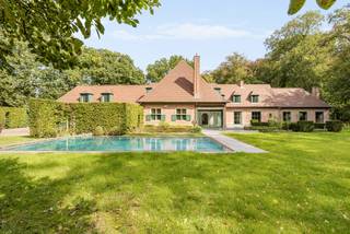 Verscholen in het groen van de gegeerde Bellevuedreef bevindt zich deze karaktervolle klassieke villa op een indrukwekkend parkdomein van ca. 1,4 hectare. Een eigendom waar ruimte, privacy en een bijzonder aangename woonbeleving samenkomen, omgeven door een volgroeide en zorgvuldig aangelegde tuin.<br /><br />De villa beschikt over ca. 575 m² bewoonbare oppervlakte en wordt aangevuld met een volwaardig gastenverblijf in het poolhouse, een afzonderlijke conciërgewoning, een inpandige garage voor drie wagens en een verwarmd buitenzwembad. De omvang van het domein, de volwassen begroeiing en de verschillende woon- en verblijfsfuncties maken van deze eigendom een bijzonder compleet geheel op een van de meest residentiële locaties van Schilde.<br /><br />Indeling gelijkvloers:<br />De centrale inkomhal met vestiaire en gastentoilet vormt het vertrekpunt van de woning en geeft toegang tot de verschillende leefruimtes.<br />De royale leefruimte omvat een zitkamer en eetkamer, aansluitend op een afzonderlijke studeerkamer. Daarnaast bevindt zich een ruim bureel met maatwerkkasten, waardoor ook professioneel of rustig thuiswerken perfect in de woning kan worden geïntegreerd.<br />Centraal in het dagelijkse leven staat de ruime leefkeuken, opgebouwd rond een gezellige ontbijtruimte met grote schuiframen naar het terras en de tuin. Het keukengedeelte met eiland is uitgerust met diverse inbouwtoestellen. Een praktische berging zorgt voor een tweede verbinding met de eetkamer, terwijl de bijkeuken met afzonderlijke zij-ingang bijkomende functionaliteit biedt.<br /><br />Eerste verdieping:<br />De nachthal leidt naar vier ruime slaapkamers, die elk over een eigen badkamer beschikken.<br />De mastersuite vormt een royaal privégedeelte met slaapkamer, dressing en badkamer. Daarnaast bevinden zich op deze verdieping een tweede ruime slaapkamer, een gastenkamer en een kinderkamer, telkens met een eigen badkamer.<br /><br />Vanuit de mastersuite is er via een tussengang en diensttrap verbinding met het gedeelte boven de garage.<br /><br />Conciërgewoning:<br />Boven de inpandige garage bevindt zich een afzonderlijk verblijfs- en conciërgegedeelte, bestaande uit een polyvalente leefruimte, slaapkamer en badkamer. Dit gedeelte leent zich uitstekend voor inwonend personeel, een au pair, familie of gasten.<br /><br />Kelder:<br />Via een natuurstenen trap is de kelderverdieping bereikbaar. Hier bevinden zich bijkomende bergruimtes, de technische installaties voor de woning en het zwembad en een sfeervolle wijnkelder.<br /><br />Poolhouse &amp; gastenverblijf:<br />Aan het verwarmde zwembad bevindt zich een royaal bijgebouw, architecturaal afgestemd op de hoofdwoning. Het poolhouse werd ingericht als een volwaardig zelfstandig gastenverblijf met woonkamer, keuken, slaapkamer en badkamer.<br />Samen met de omliggende terrassen en het zwembad ontstaat hier een bijzonder aangename omgeving voor ontspanning, familie en gasten, met een grote mate van privacy ten opzichte van de hoofdwoning.<br /><br />Bijzonderheden:<br />- Uitzonderlijk parkdomein van ca. 14.433 m²<br />- Volledig omheind domein met maximale privacy<br />- Volgroeide tuin met uitgestrekte gazons en volwassen bomen<br />- Regelmatig onderhouden en verder opgefrist<br />- Verwarmd buitenzwembad<br />- Volwaardig poolhouse ingericht als zelfstandig gastenverblijf<br />- Afzonderlijk conciërge- of personeelsverblijf<br />- Inpandige garage voor drie wagens<br />- Verschillende ruime terrassen rondom de woning<br />- Uitgebreide tuinverlichting<br />- Alarm- en camerabewaking<br /><br />Een bijzonder compleet residentieel domein waar ruimte, discretie en groen centraal staan, op een van de meest gewaardeerde locaties van Schilde.