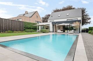 <p><span>Villa de luxe avec piscine et pool house à proximité du centre de Hoogstraten</span></p><p><span>Située dans un endroit calme mais central, à proximité du centre de Hoogstraten, cette spacieuse villa a été entièrement rénovée en 2019 pour offrir un état neuf. Cette demeure étonnamment spacieuse offre environ 425 m² de surface habitable !</span></p><p><span> </span></p><p><span>Agencement</span></p><p><span>Vous entrez dans la maison par le hall d'entrée, qui comprend des toilettes pour invités et un escalier menant à l'étage. Dès votre arrivée, une grande porte vitrée vous offre une vue dégagée sur le jardin. Depuis le hall d'entrée, vous accédez également à un espace bureau situé à l'avant de la maison. Le très spacieux espace de vie offre une vue magnifique sur le jardin et bénéficie d’une abondante lumière naturelle. Côté rue, il comprend une salle de jeux ou un deuxième bureau, un coin salon avec une cheminée à gaz, une salle à manger centrale et une cuisine ouverte dotée d’un grand îlot avec un coin petit-déjeuner. La cuisine bénéficie de finitions haut de gamme et est équipée de divers appareils encastrés. Depuis la cuisine, un passage mène à l’arrière-cuisine et à la buanderie, et permet d’accéder à la cave avec un espace de rangement supplémentaire.</span></p><p><span> </span></p><p><span>Étage</span></p><p><span>Un escalier moderne doté d’un éclairage indirect mène au couloir de nuit donnant accès à la spacieuse suite parentale composée d’une chambre, d’un dressing avec placards intégrés et d’une salle de bains spacieuse. On y trouve également deux chambres d’enfants très spacieuses avec placards intégrés et une deuxième salle de bains. Toutes les chambres sont équipées de volets roulants.</span></p><p><span> </span></p><p><span>Deuxième étage</span></p><p><span>Le deuxième étage a également été entièrement aménagé et fini ; il comprend un vaste espace polyvalent qui sert actuellement de bureau, ainsi qu’un grenier de rangement et un local technique.</span></p><p><span> </span></p><p><span>Sous-sol</span></p><p><span>Depuis l'arrière-cuisine, vous accédez au sous-sol qui vous offre un espace de rangement supplémentaire au frais.</span></p><p><span> </span></p><p><span>Pool house</span></p><p><span>Le pool house indépendant offre un espace multifonctionnel pouvant servir de salle de détente, de salle de fête ou de salle de sport. Il dispose de divers équipements, notamment une cuisine équipée avec divers appareils (lave-vaisselle, four, réfrigérateur avec congélateur), ainsi que des sanitaires avec douche et toilettes.</span></p><p><span> </span></p><p><span>Jardin, piscine et espaces extérieurs</span></p><p><span>Le magnifique jardin aménagé bénéficie d’une exposition sud et d’une grande intimité ; les spacieuses terrasses entourant la piscine chauffée offrent suffisamment d’espace pour installer des chaises longues et du mobilier de jardin. Au fond du jardin, un espace de jeux est prévu pour les enfants.</span></p><p><span> </span></p><p><span>Parking, garage et abri pour voiture</span></p><p><span>Des places de stationnement équipées d’une infrastructure de recharge pour véhicules électriques ont été prévues à côté et devant la villa. Il est possible d’aménager un garage intégré pouvant accueillir une voiture, ainsi qu’un abri de voiture sur le côté de la villa. Pour plus d’informations à ce sujet, veuillez contacter notre agence.</span></p><p><span> </span></p><p><span>Particularités</span></p><p><span>Cette spacieuse demeure est à la pointe de la technologie et a été entièrement rénovée en 2019 pour retrouver l’état d’une construction neuve. La villa est équipée d’un système domotique, d’un chauffage au sol avec pompe à chaleur (géothermie) ainsi que d’un système de refroidissement passif au rez-de-chaussée et au 1er étage. Puits foré, arrosage du jardin, jardin clôturé avec terrasses, piscine chauffée avec volet roulant automatique, pool house avec bar, cuisine, toilettes et douche. Système de ventilation, niveau E = 3 (maison BEN), panneaux solaires de 11 kW. Au premier étage, toutes les fenêtres sont équipées de volets roulants. Les fenêtres de la façade sud (façade arrière) ont été équipées de stores vénitiens, et un avant-toit a été aménagé pour profiter d'un ensoleillement optimal en fonction de la saison.</span></p><p><span> </span></p><p><span> </span></p>